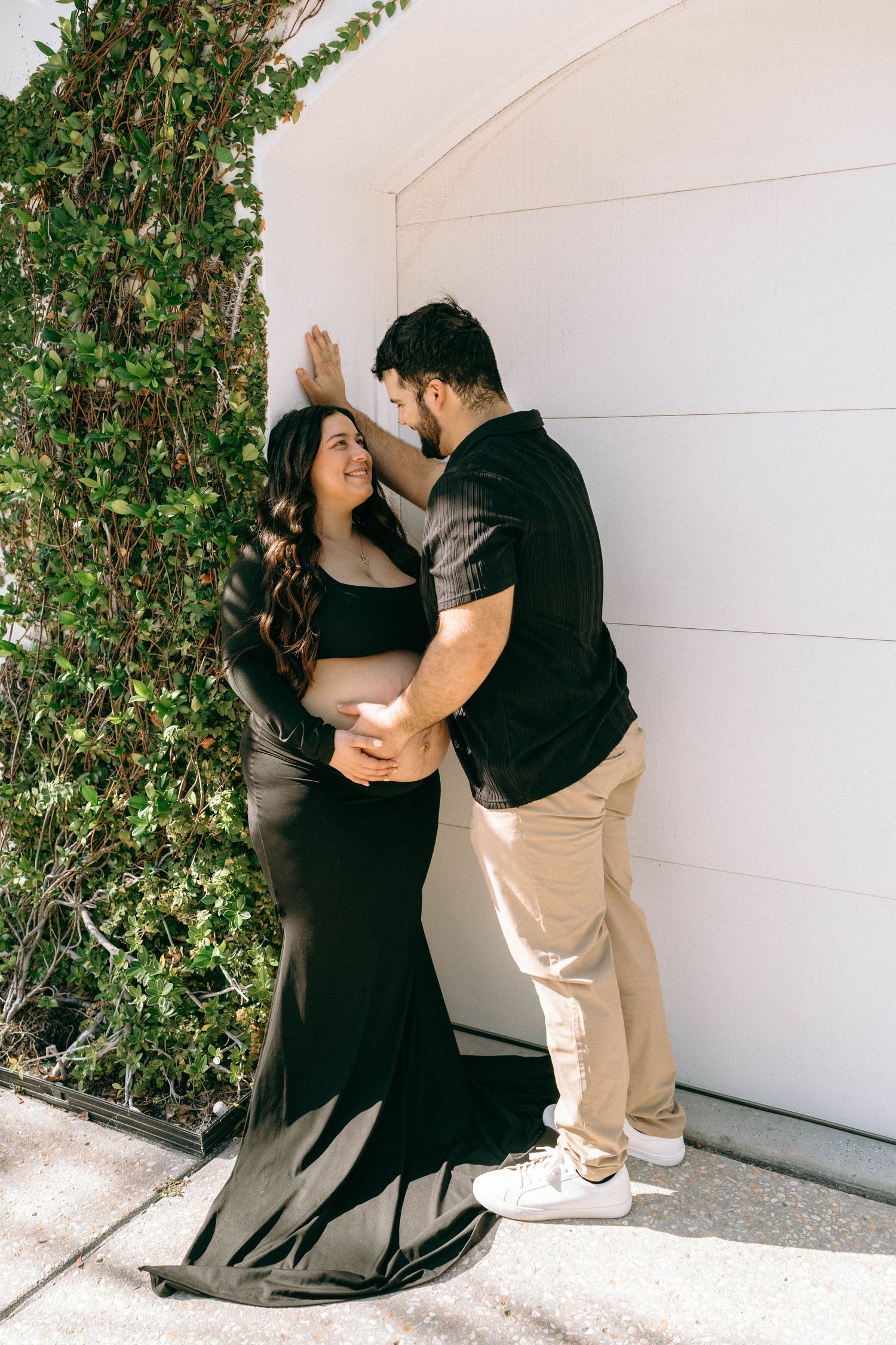 Loving couple sharing tender moment against white garage door surrounded by green ivy wall. Worth Avenue, Palm Beach, FL