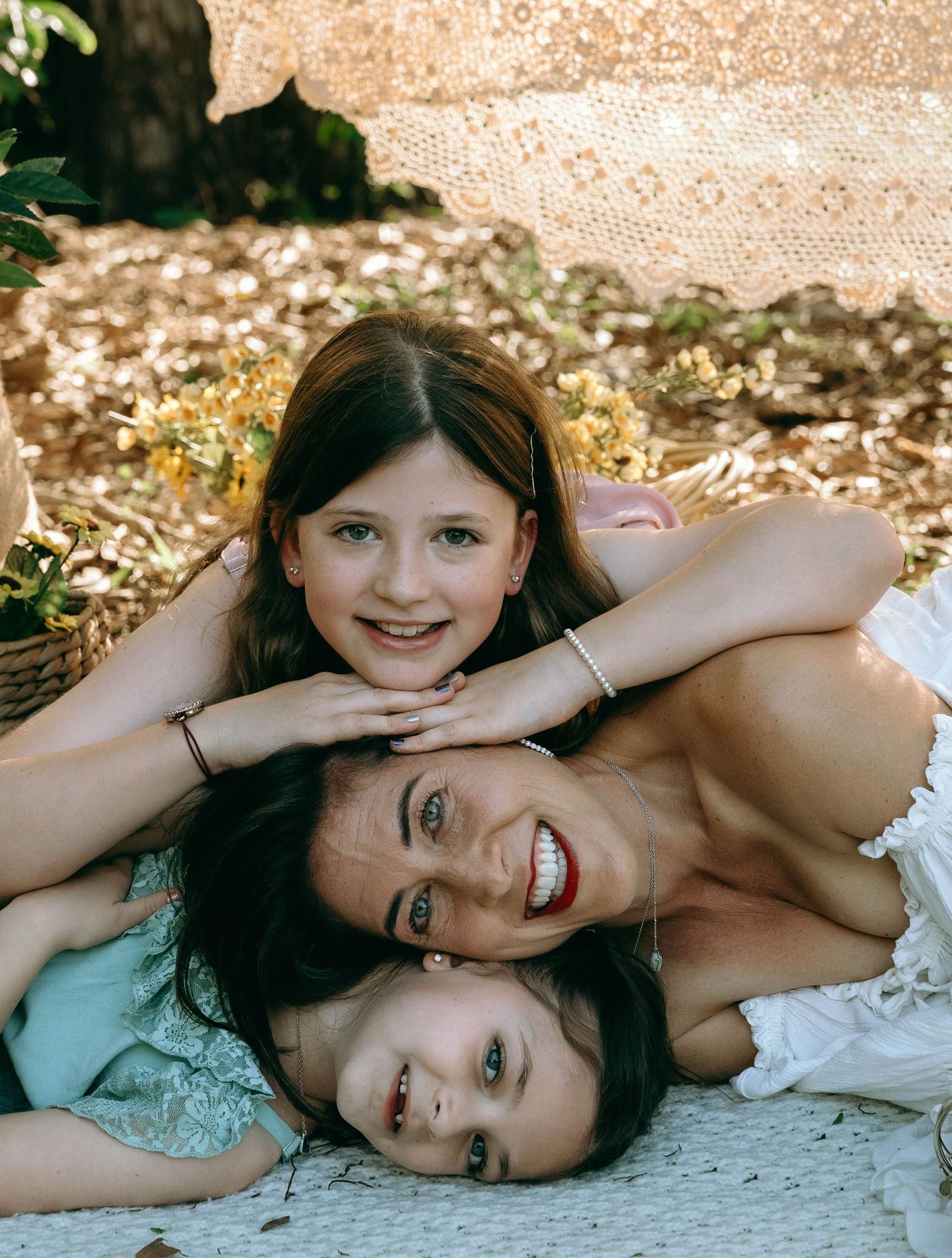 Three girls lying together outdoors on a blanket, smiling joyfully during a sunny picnic in nature. Colt Farms