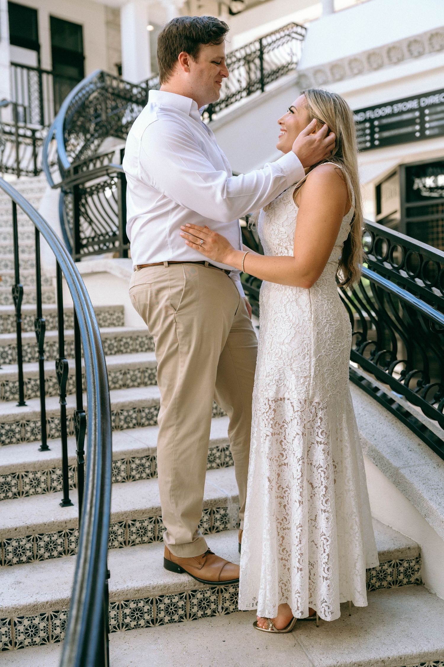 Couple in elegant attire sharing a romantic moment on decorative tiled stairs with ornate black railings.