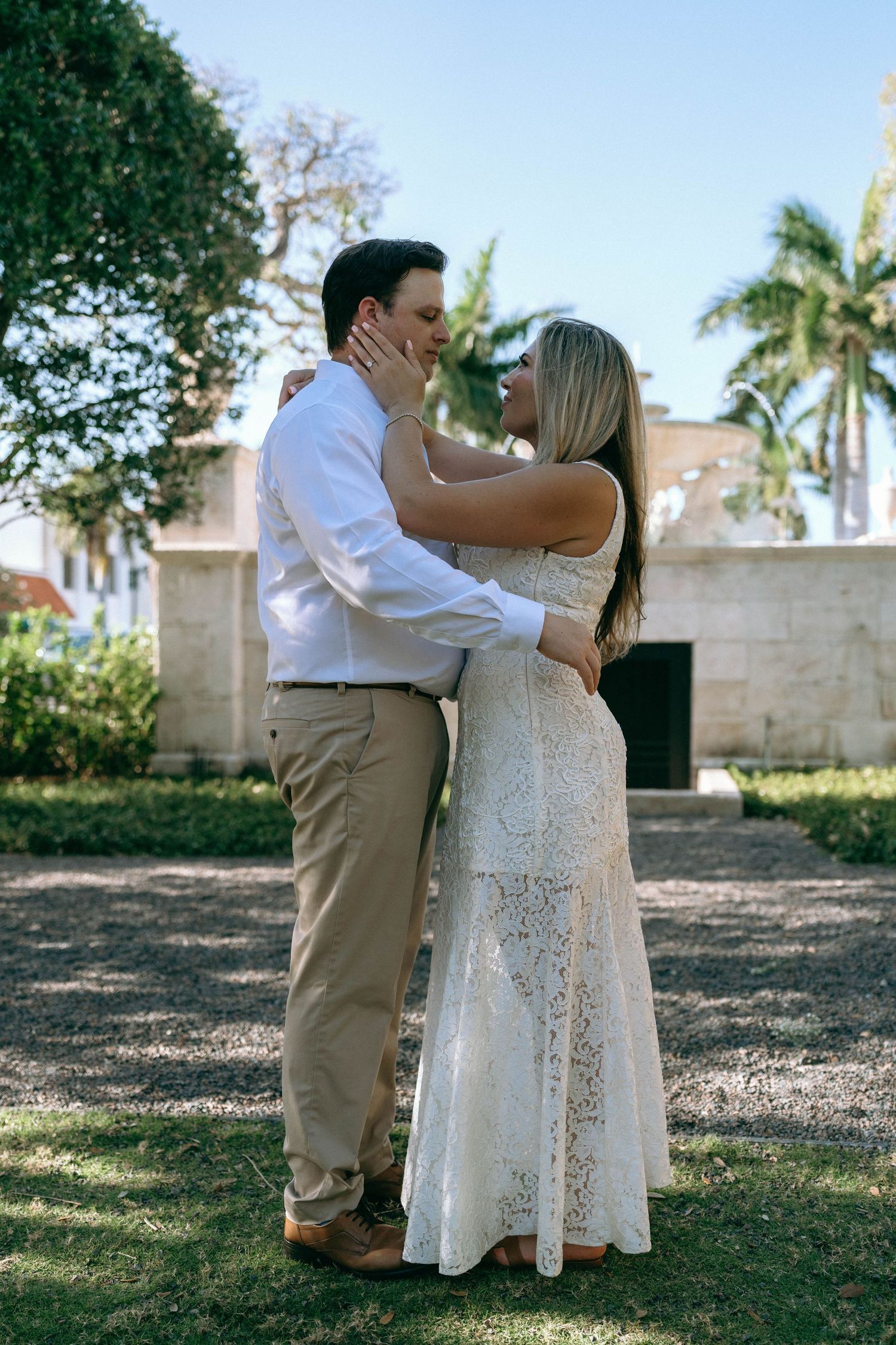 Couple embracing and kissing in a lush tropical garden, woman in white lace dress.