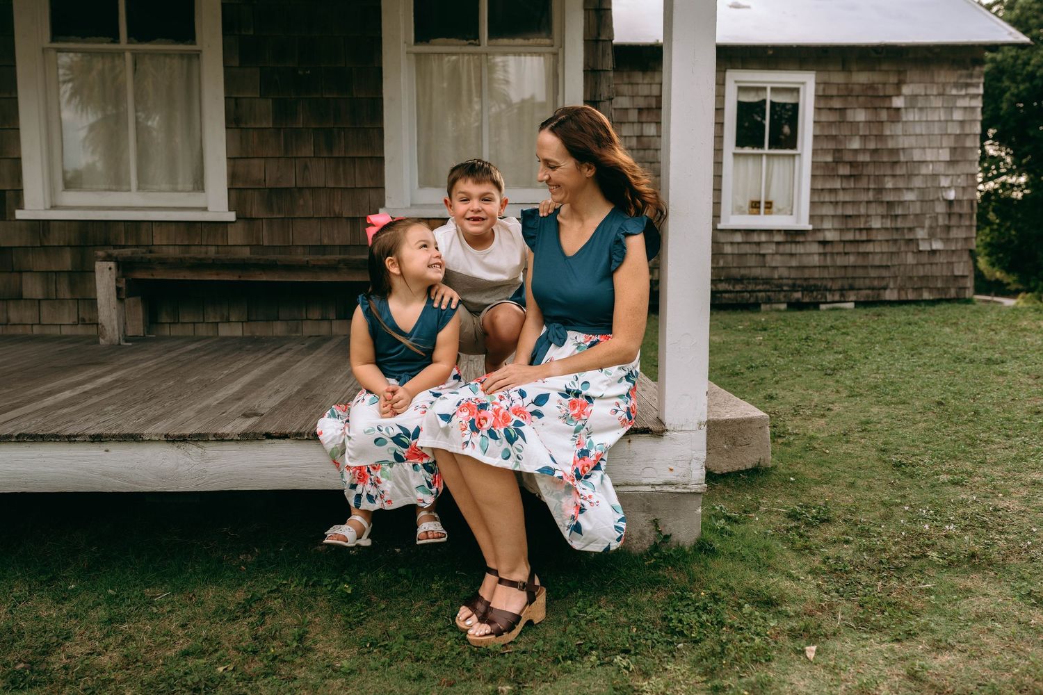 Family plays together on the front porch of a rustic shingle-sided house.