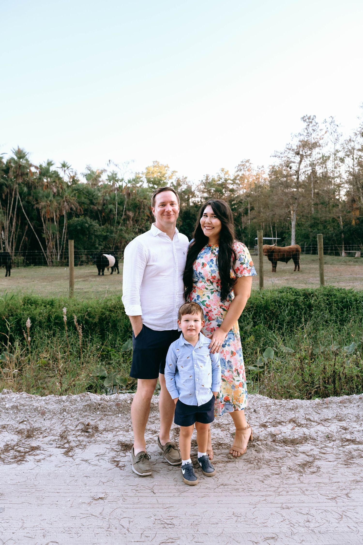 Family posing together on sandy path with trees in background during golden hour.