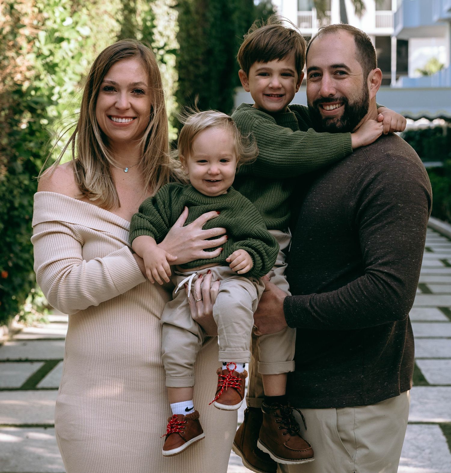 Casual family photoshoot in front of garden greenery.