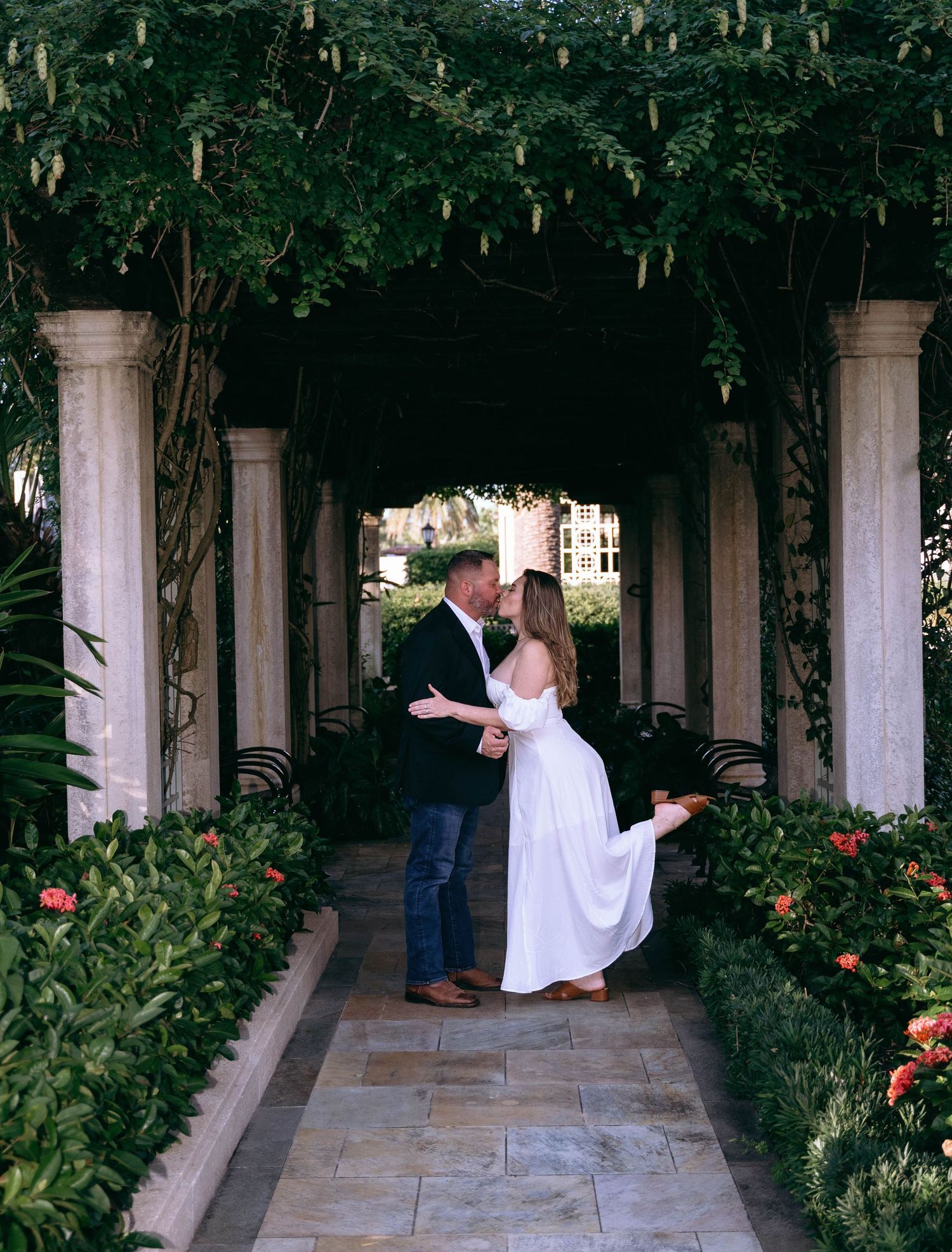 A couple embraces in a garden courtyard with columns and greenery.