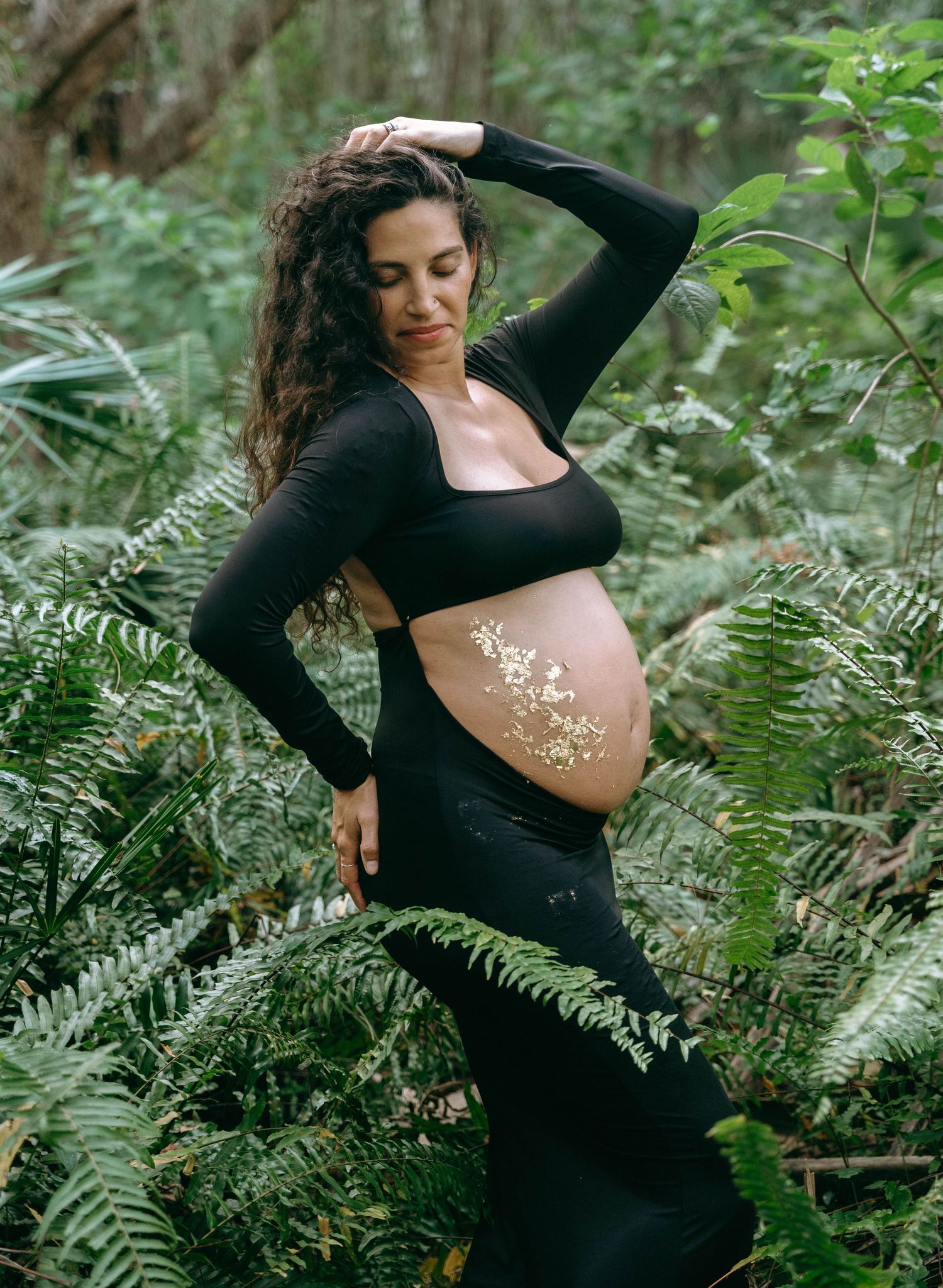 Artistic maternity photos in nature showing a figure in black among green ferns and foliage.