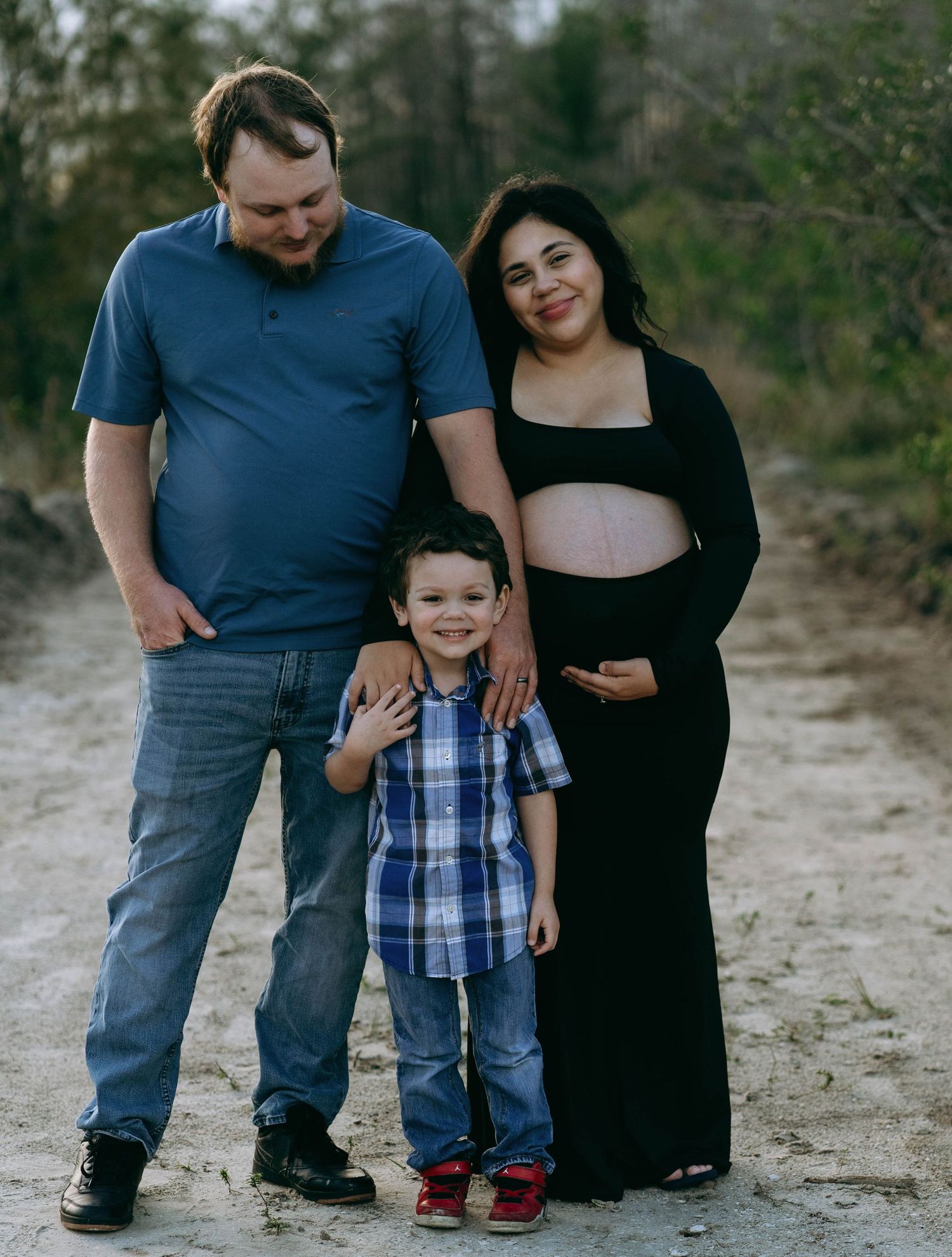 A family poses together outdoors on sandy terrain wearing casual clothing.