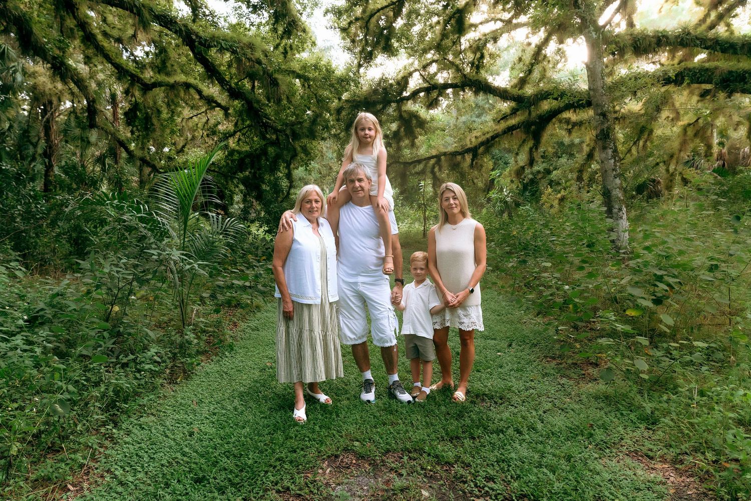 Family of five posing on a lush green path under moss-covered oak trees in a serene outdoor setting.