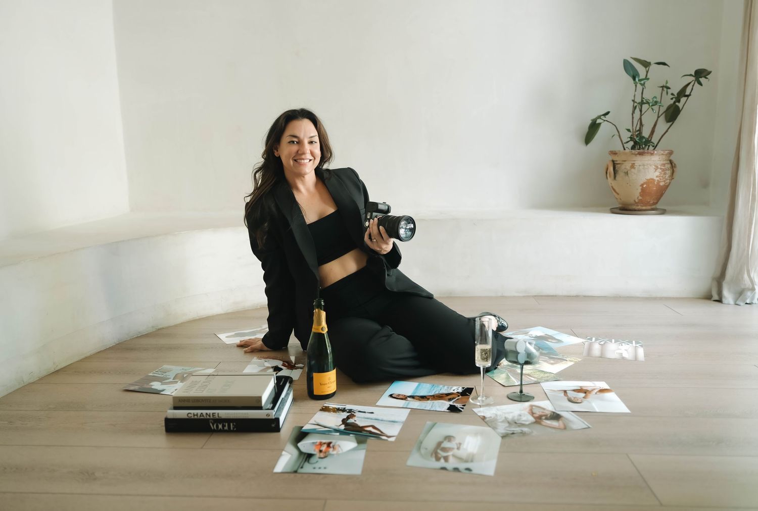 Person in black outfit lounging on wooden floor with scattered photos and a laptop nearby.