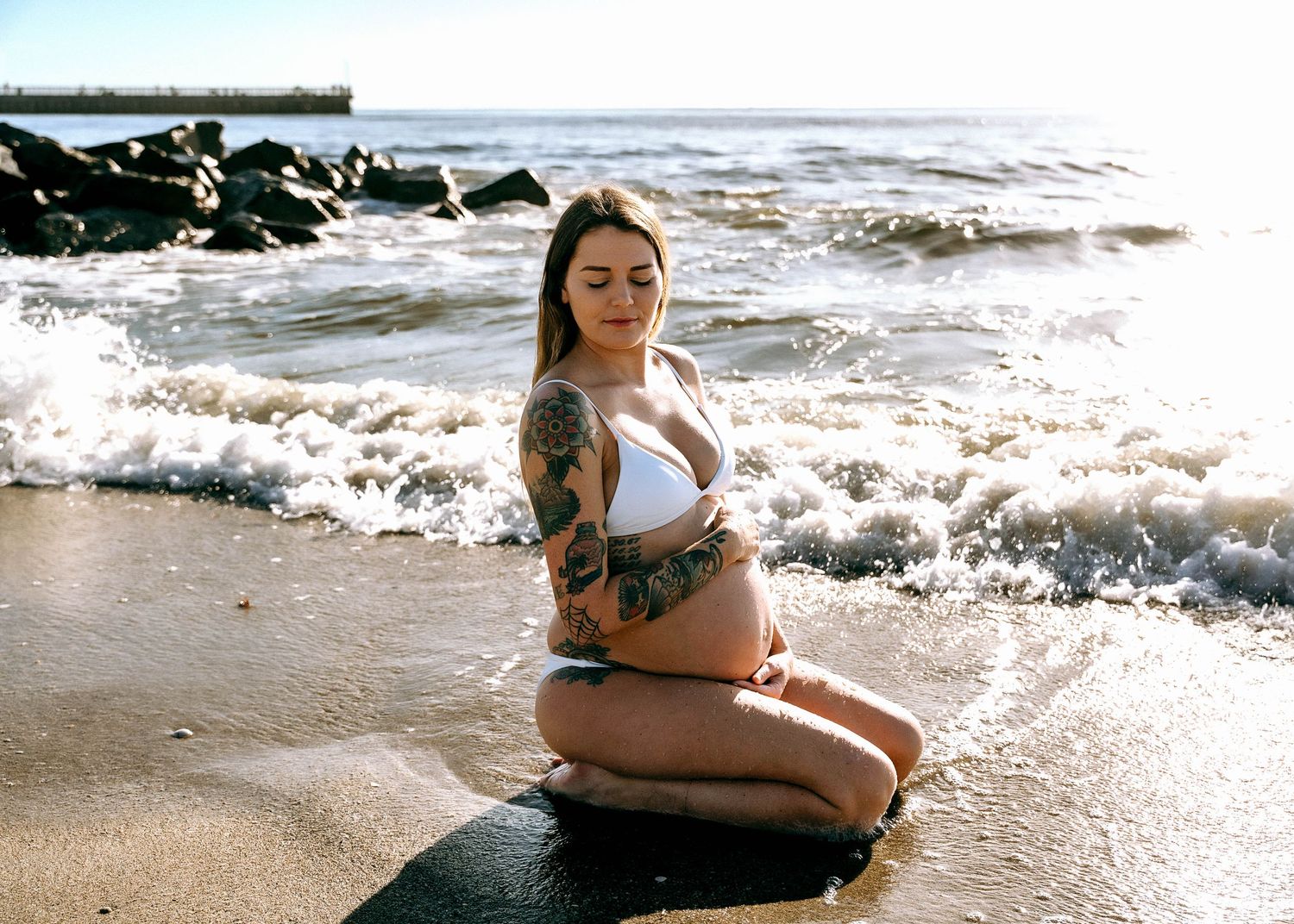 Maternity photoshoot on a rocky beach with waves crashing in the background.