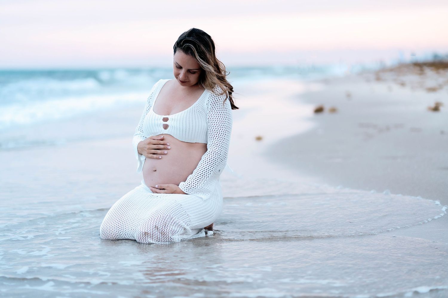 A serene maternity photoshoot at the beach with gentle waves rolling in.