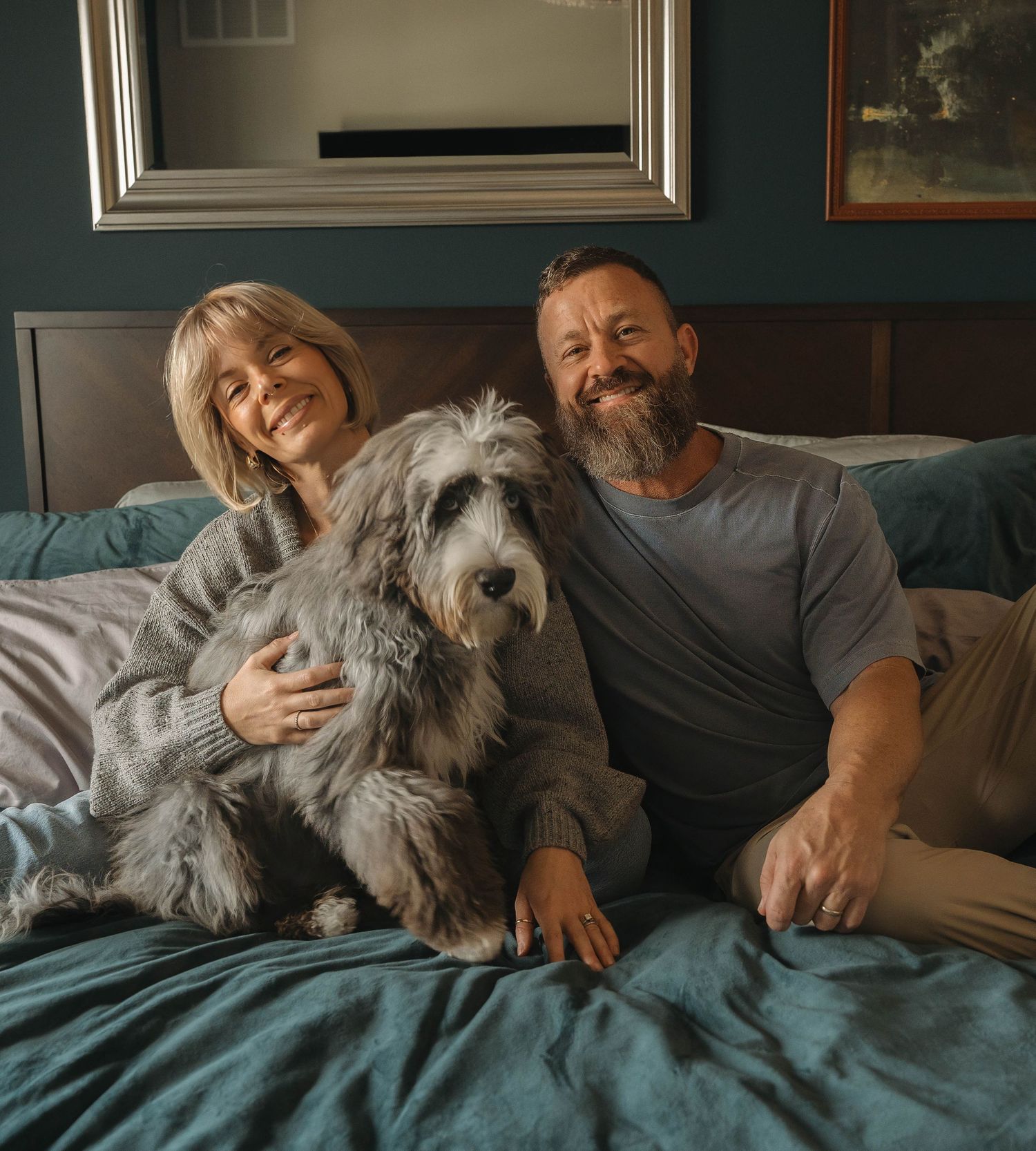 A family lounging together with their dog on a bed in a room with teal walls.