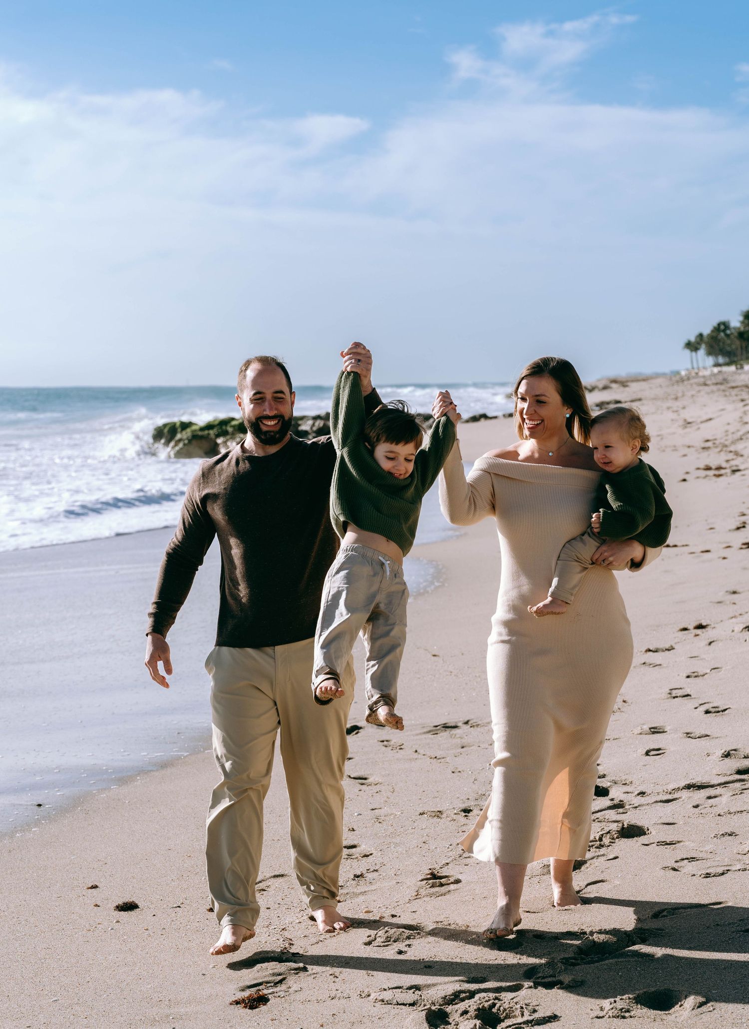 Family playing and running together on a sunny beach shoreline.