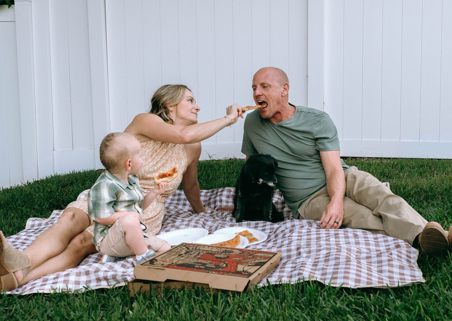 Family relaxing together on a checkered picnic blanket in the backyard.