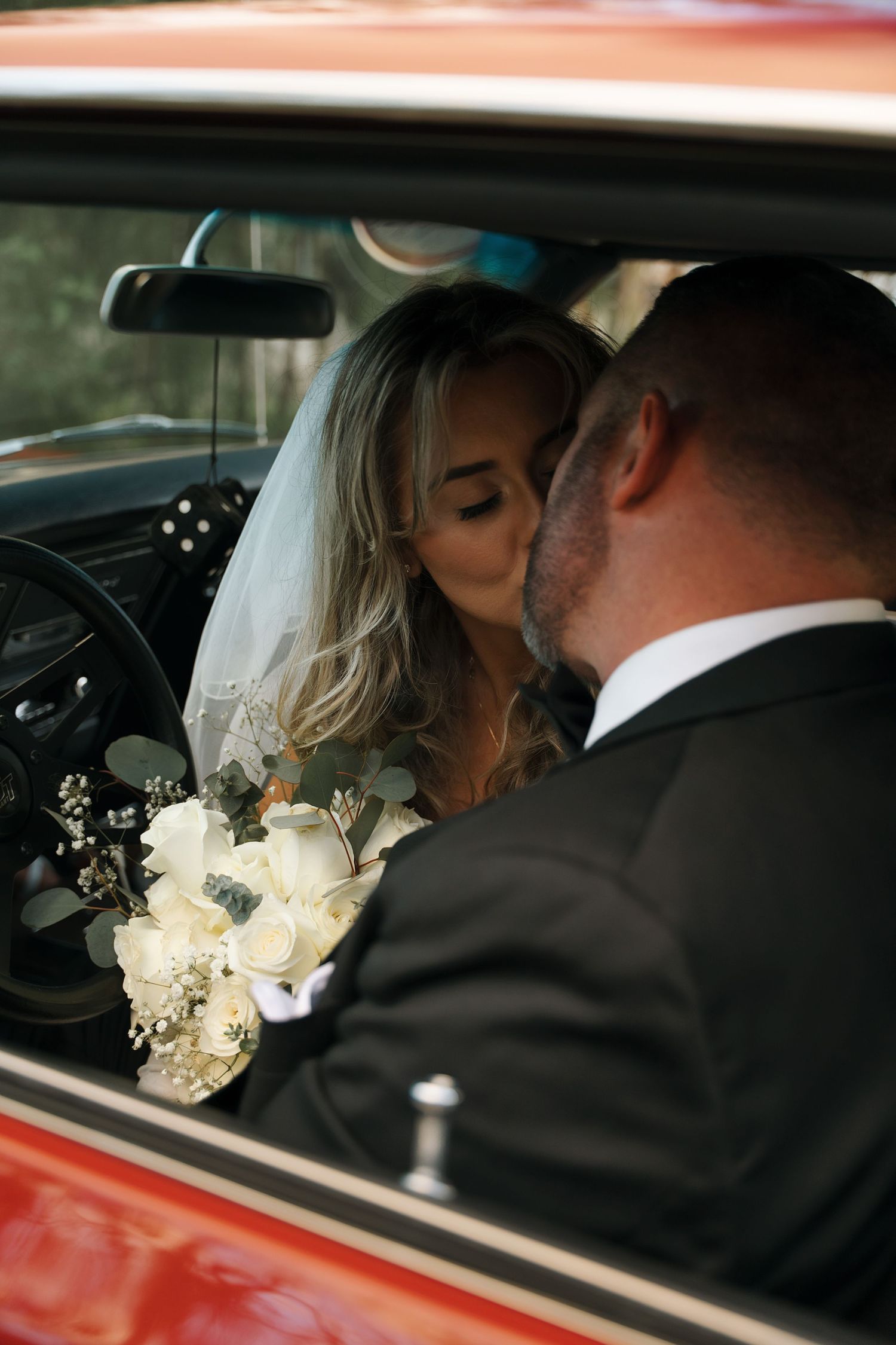 Newlyweds share tender moments inside a classic car decorated with white floral corsages.