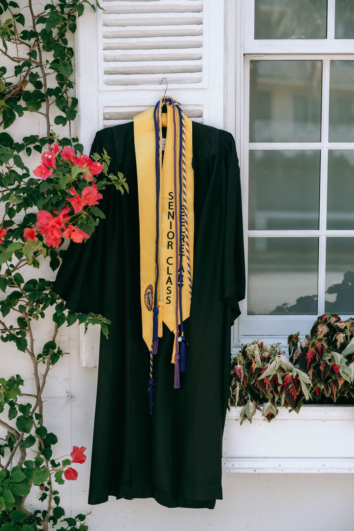 Black graduation gown with Senior Class stole hanging on white shuttered window on Worth Avenue Palm beach.