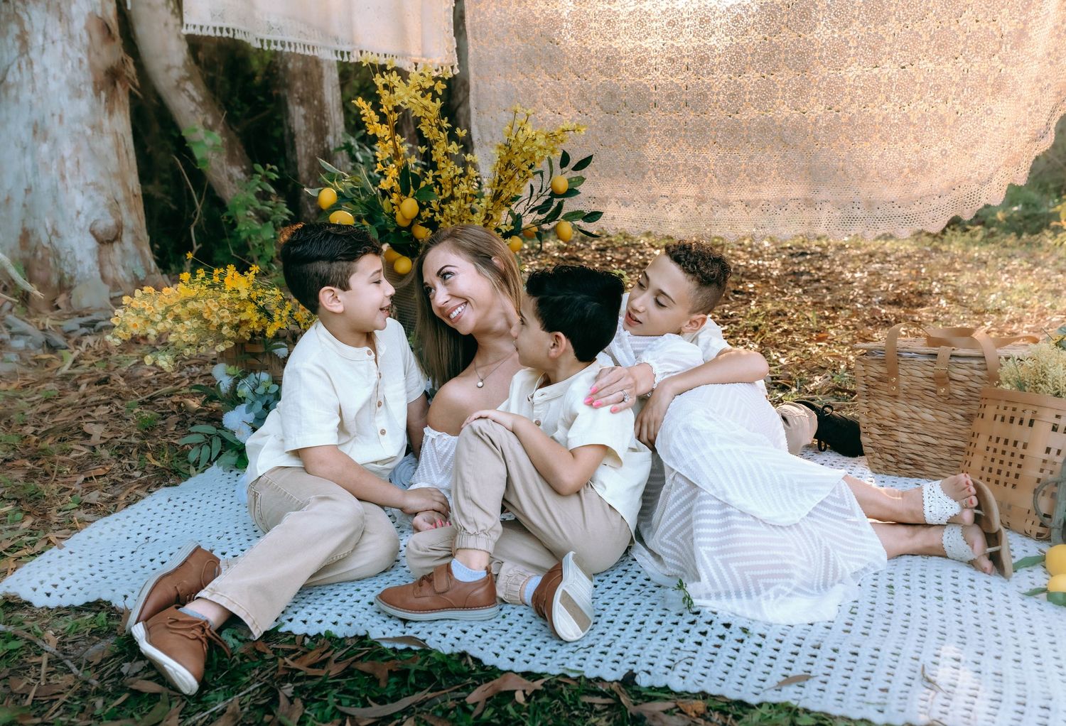 Children in white outfits lay together on a picnic blanket during an outdoor photo session.