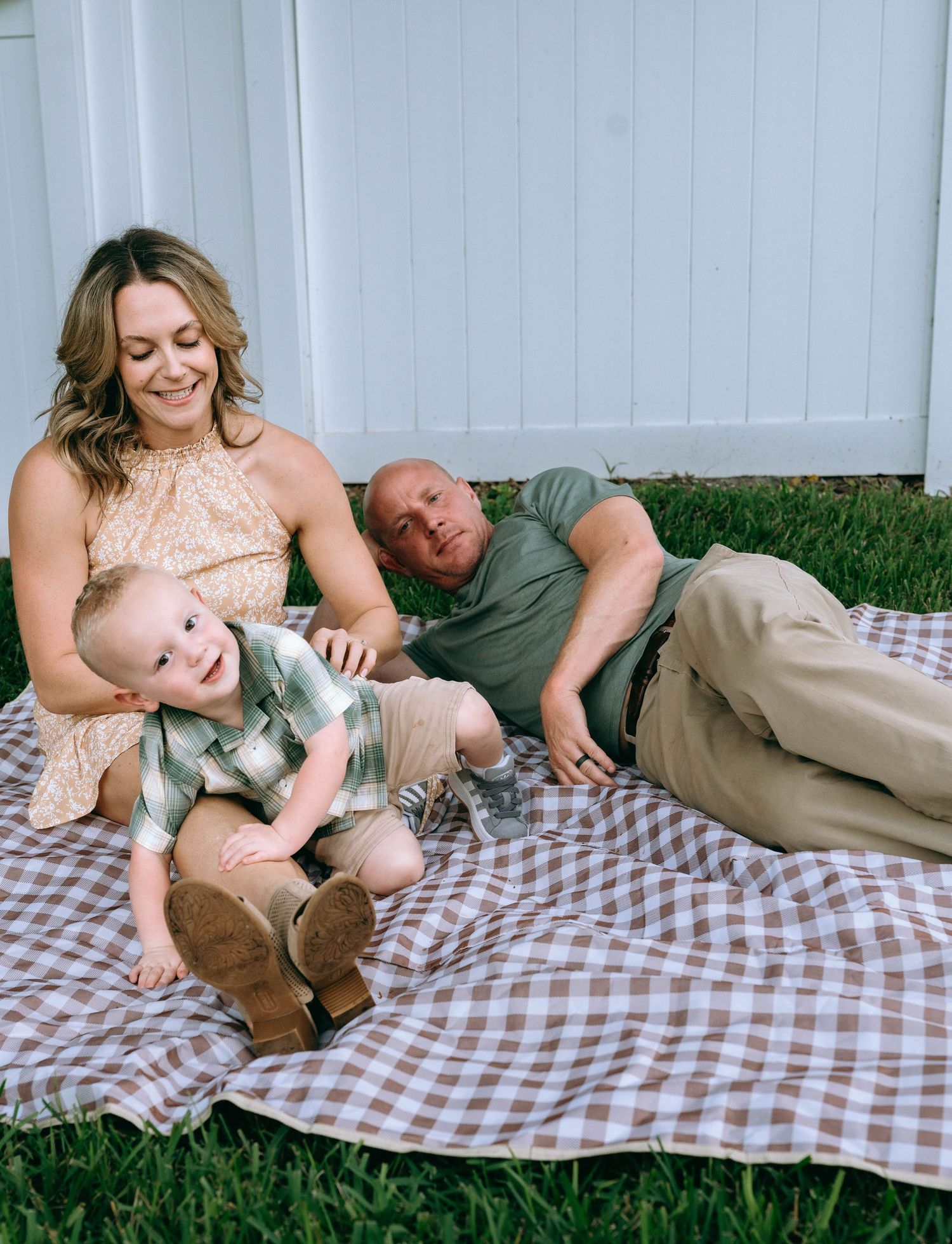 Candid family moment captured on picnic blanket against white fence.