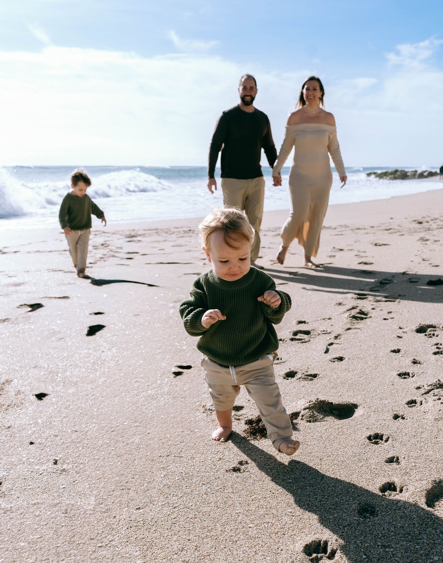 Child exploring the beach while adults walk in the background on a sunny day.