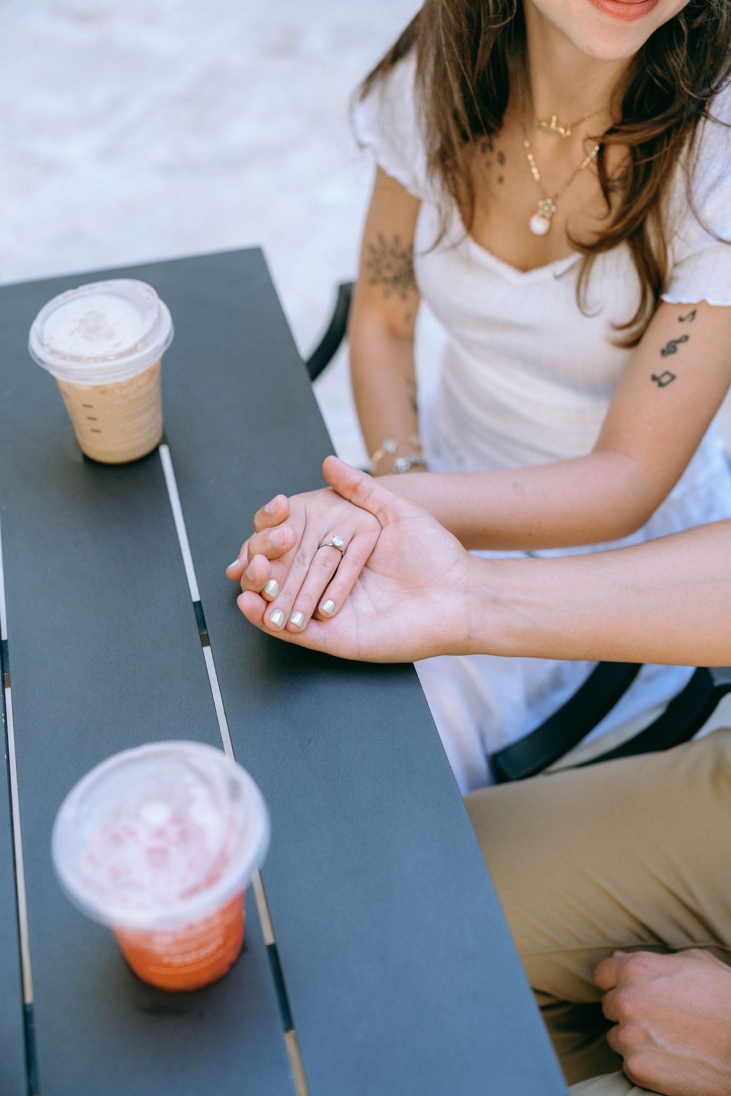Close-up of couple holding hands on outdoor cafe table with iced coffee drinks, woman wearing gold ring. Engagement photos on Worth Avenue