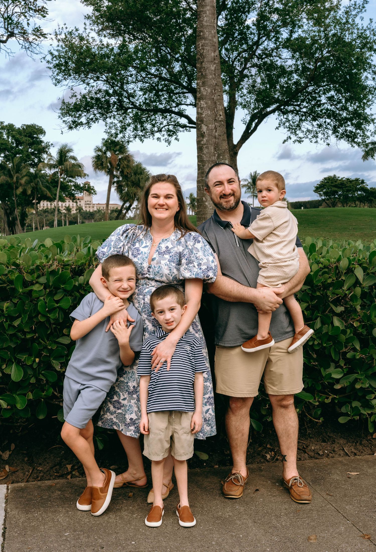 Happy family of five posing together outdoors near tropical greenery.  Family photos at Bradley Park Palm Beach, FL