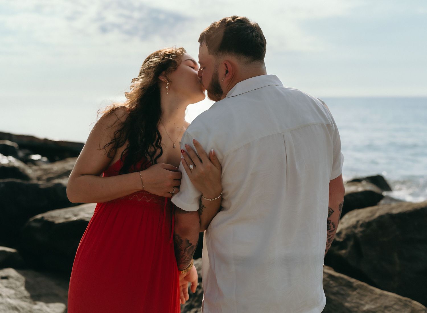 Couple sharing romantic moments on a rocky beach with ocean view.