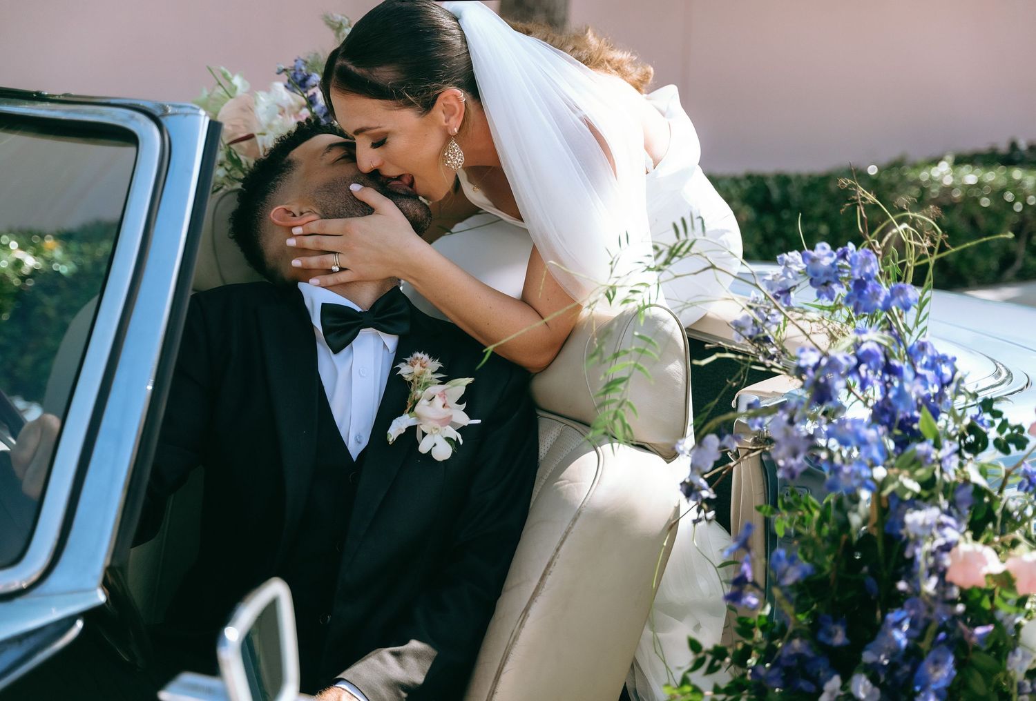 Wedding couple sharing intimate moment near car decorated with purple flowers.