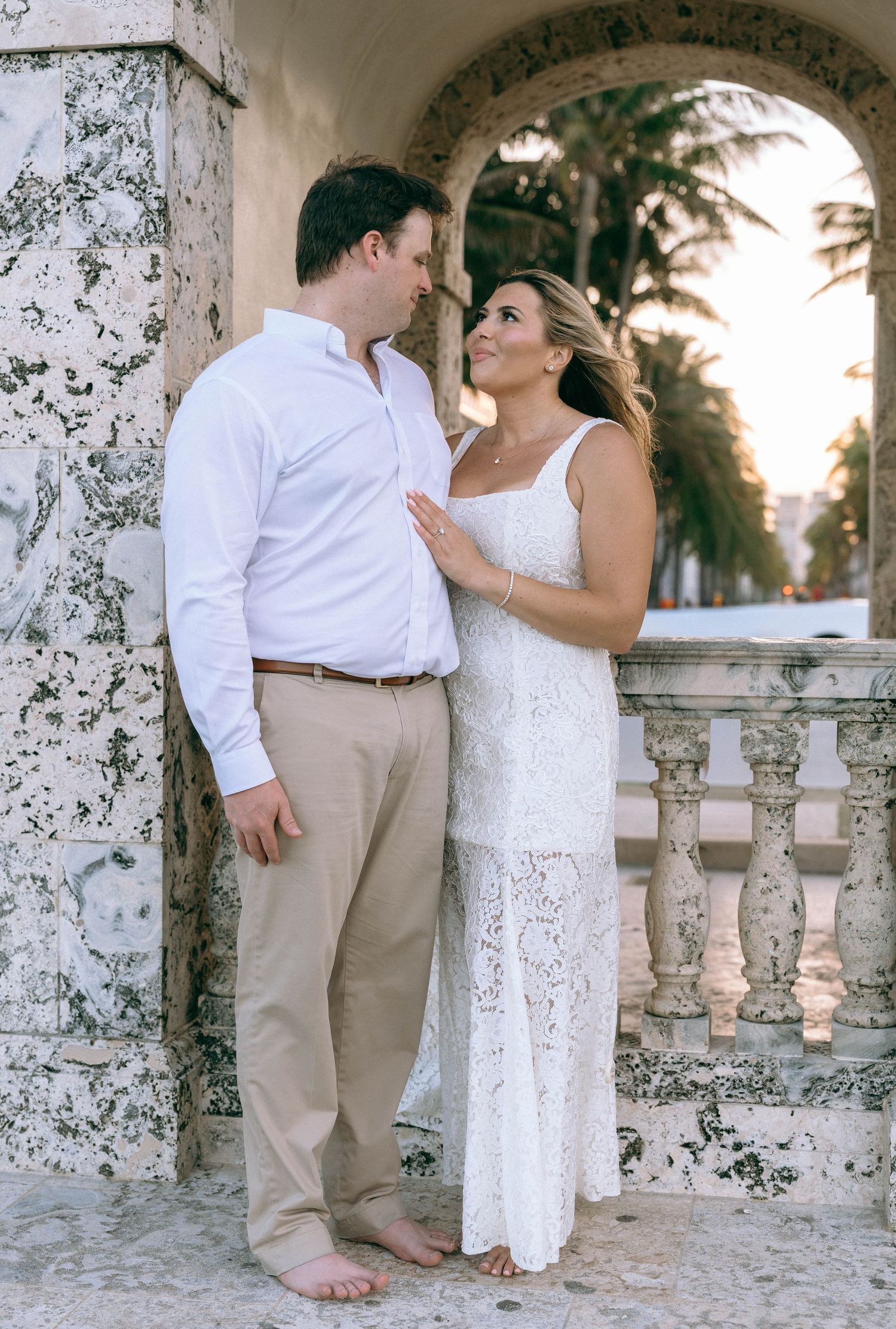 Couple in coordinating white and khaki outfits sharing a tender moment by ornate marble columns at sunset.