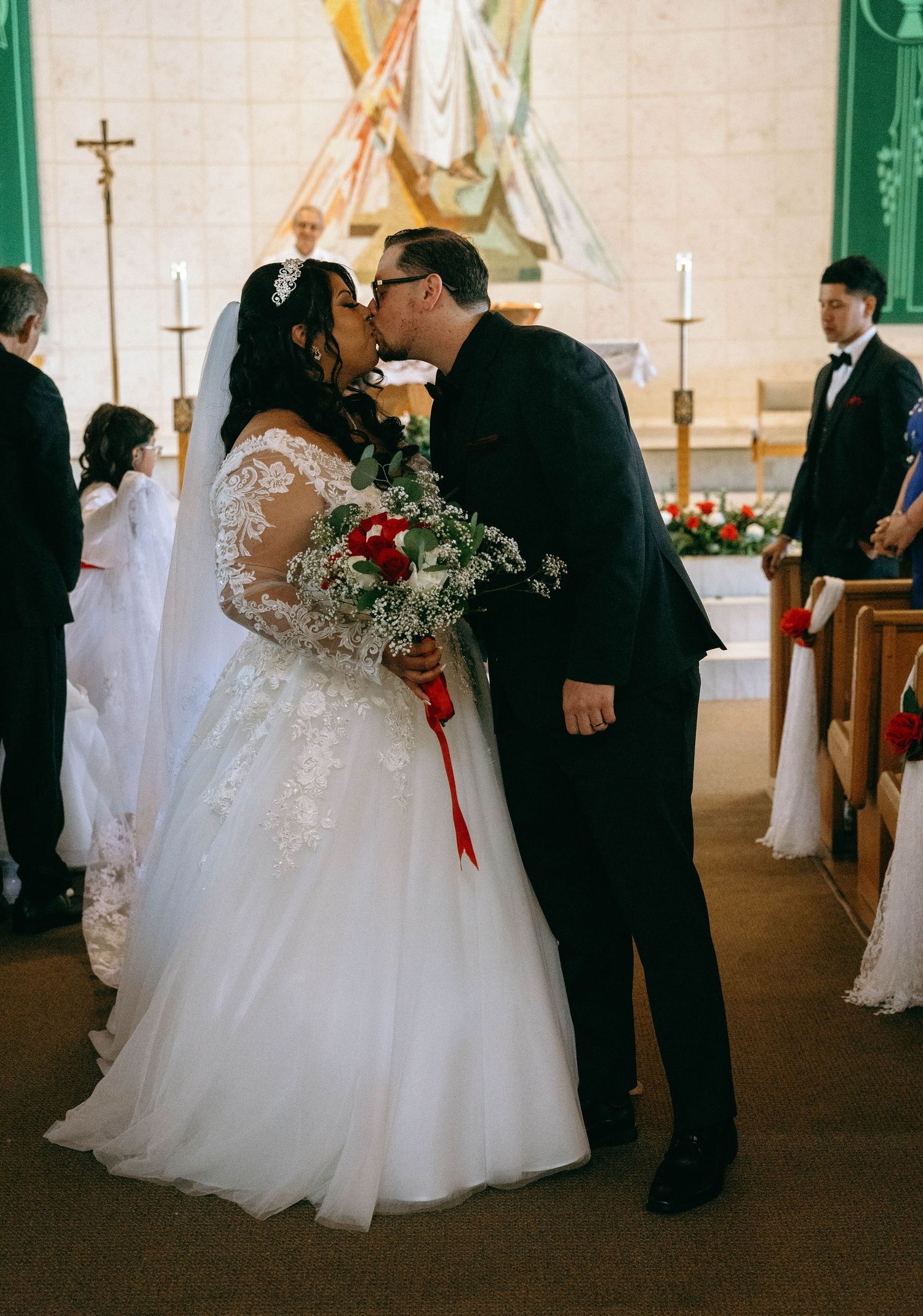 A wedding ceremony in progress inside a church with decorative green columns and crosses.