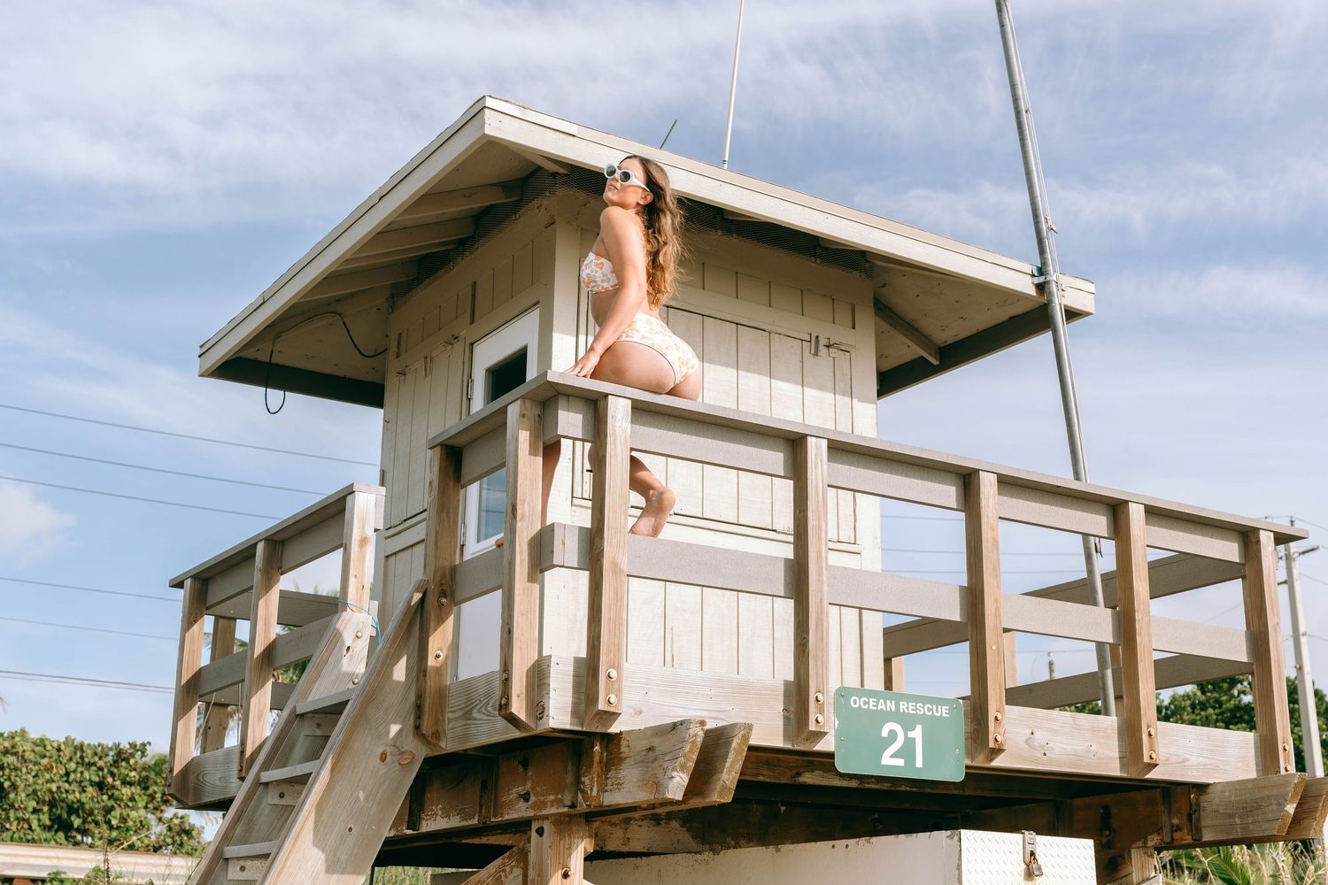 Woman posing on a wooden lifeguard tower station 21 at a sunny beach.