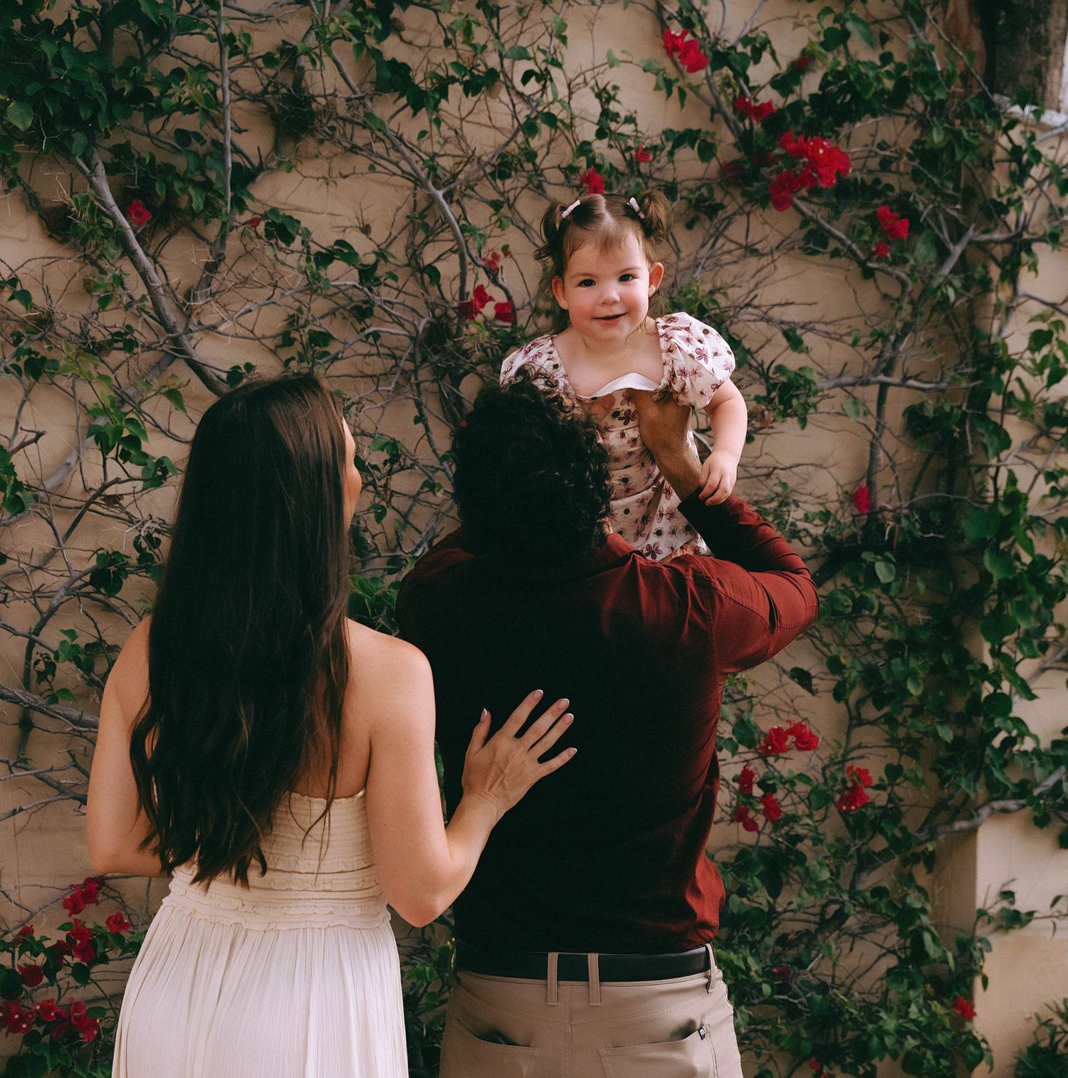 A sweet family moment captured against a wall covered in climbing roses and vines.