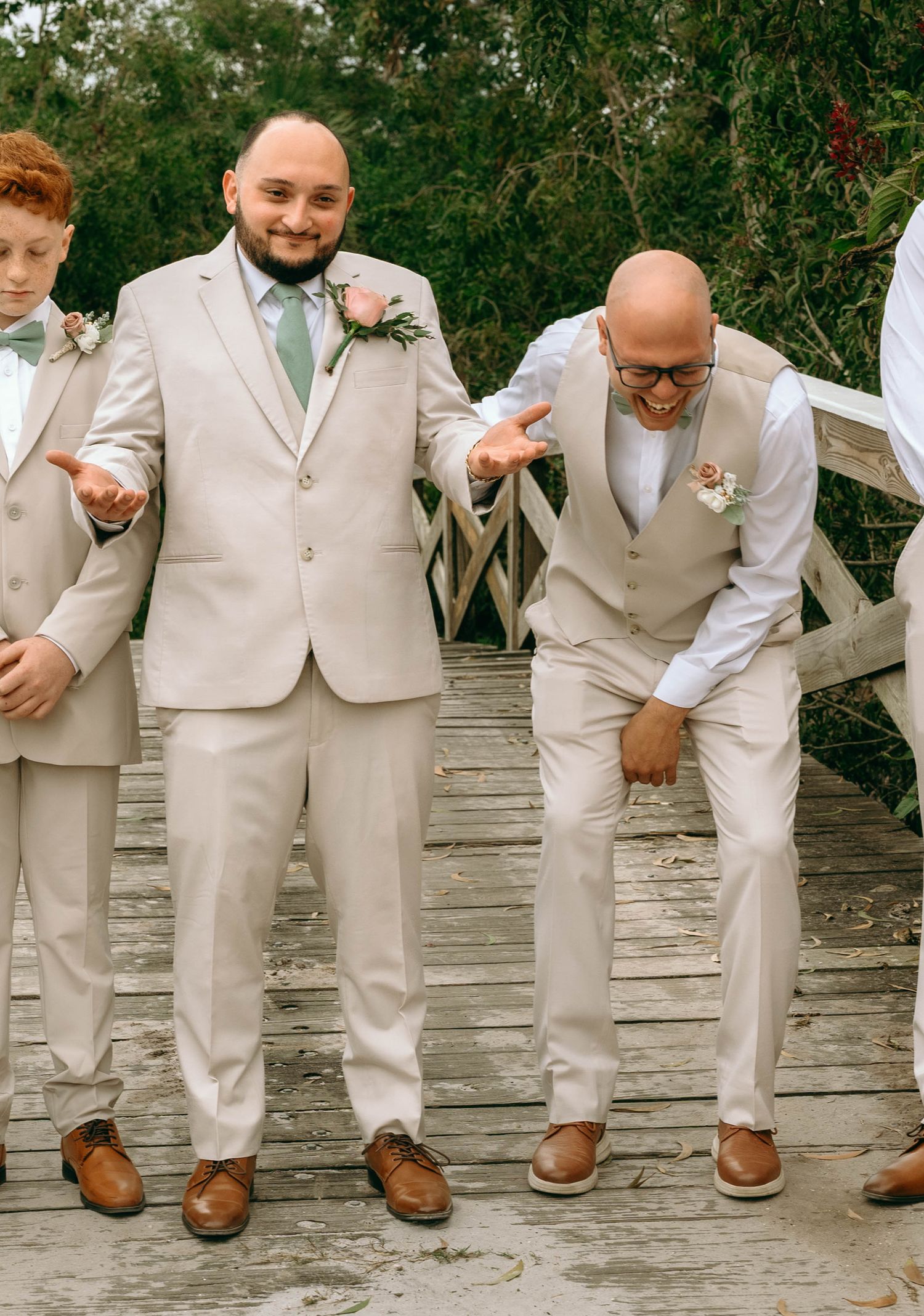 A group of groomsmen in beige suits sit on a stone wall showing off their brown leather dress shoes.