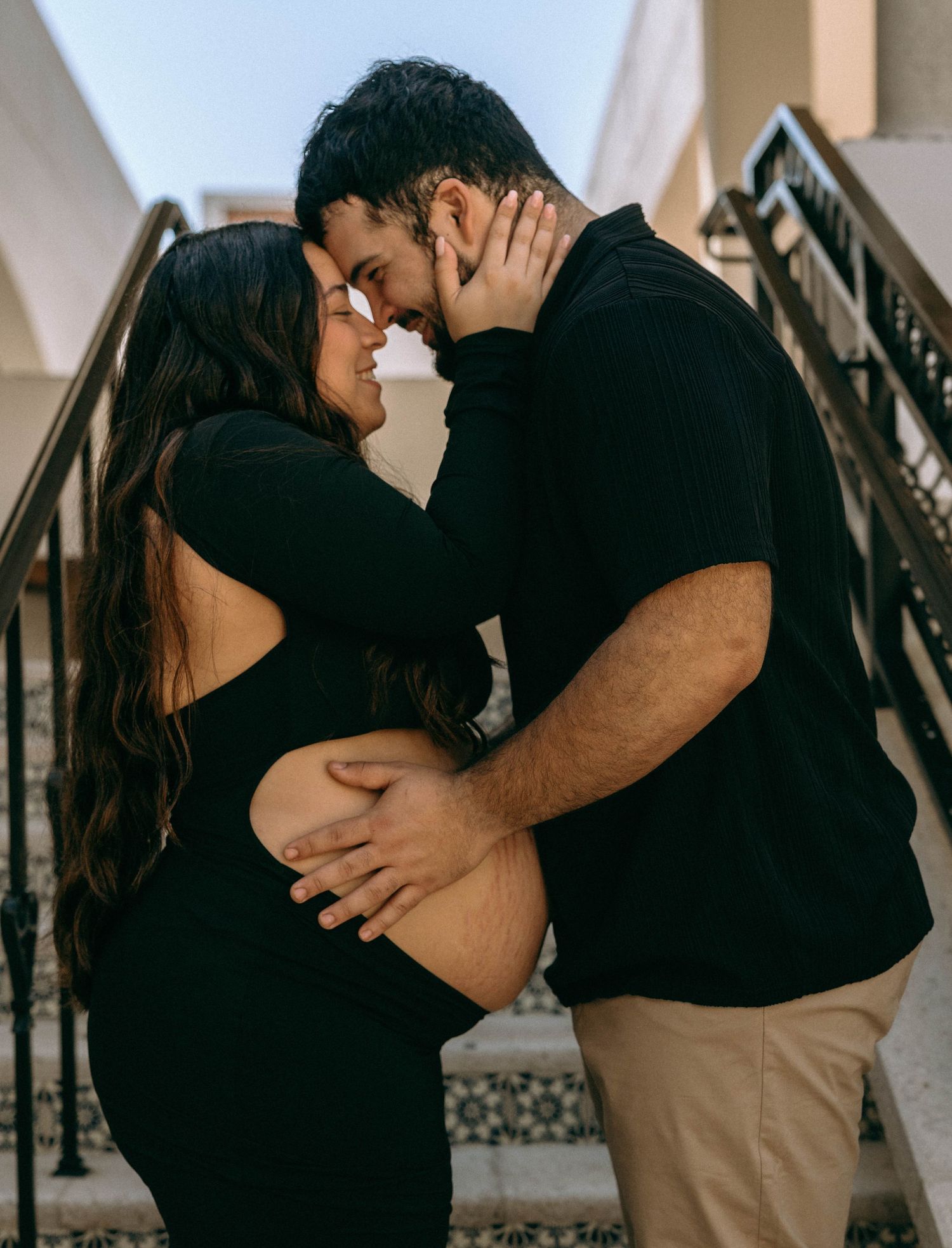 Romantic expecting couple sharing intimate moment on outdoor stairs, man tenderly holding pregnant belly. Worth Avenue, Palm Beach, FL
