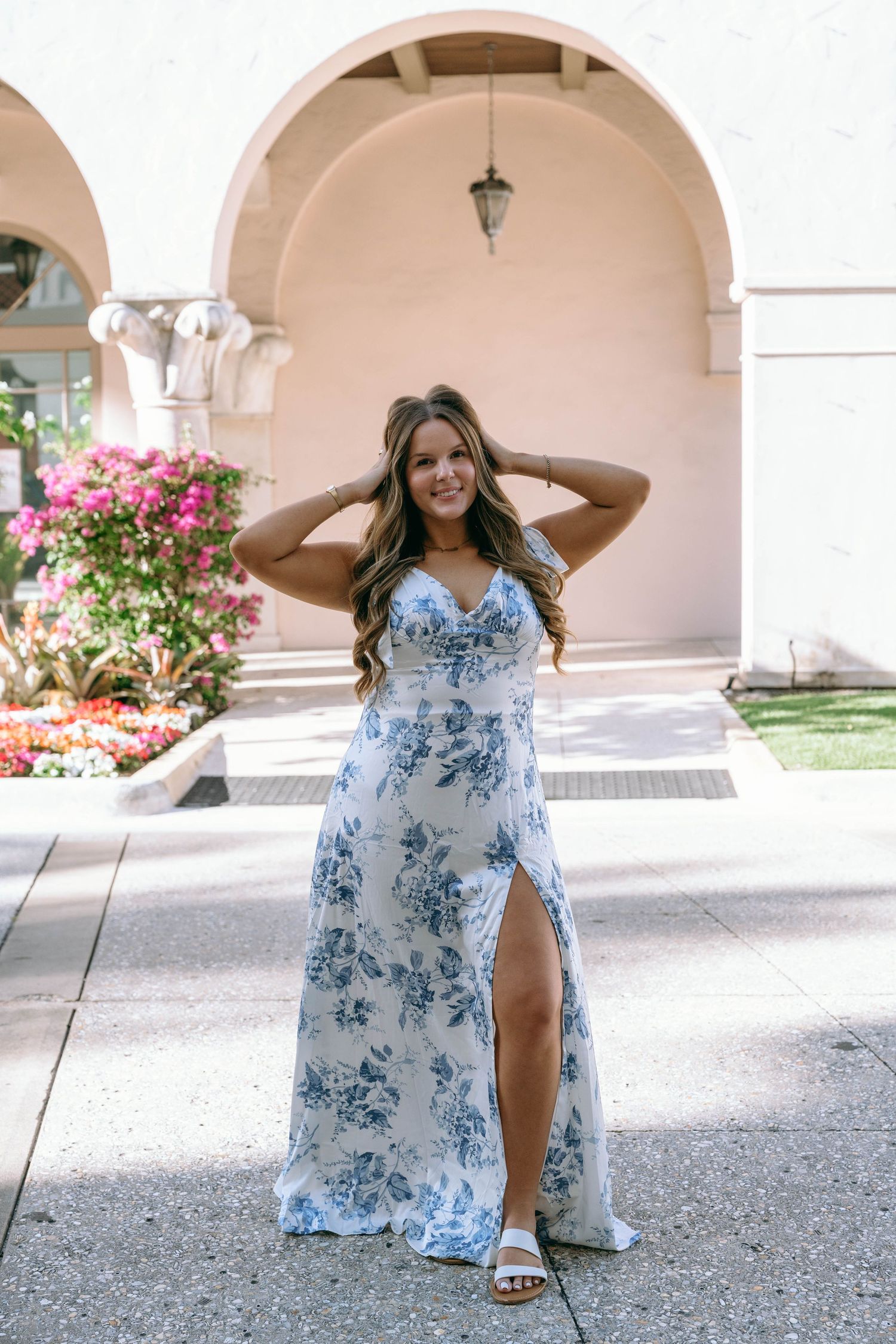 Woman in white and blue floral maxi dress with slit posing at a courtyard.