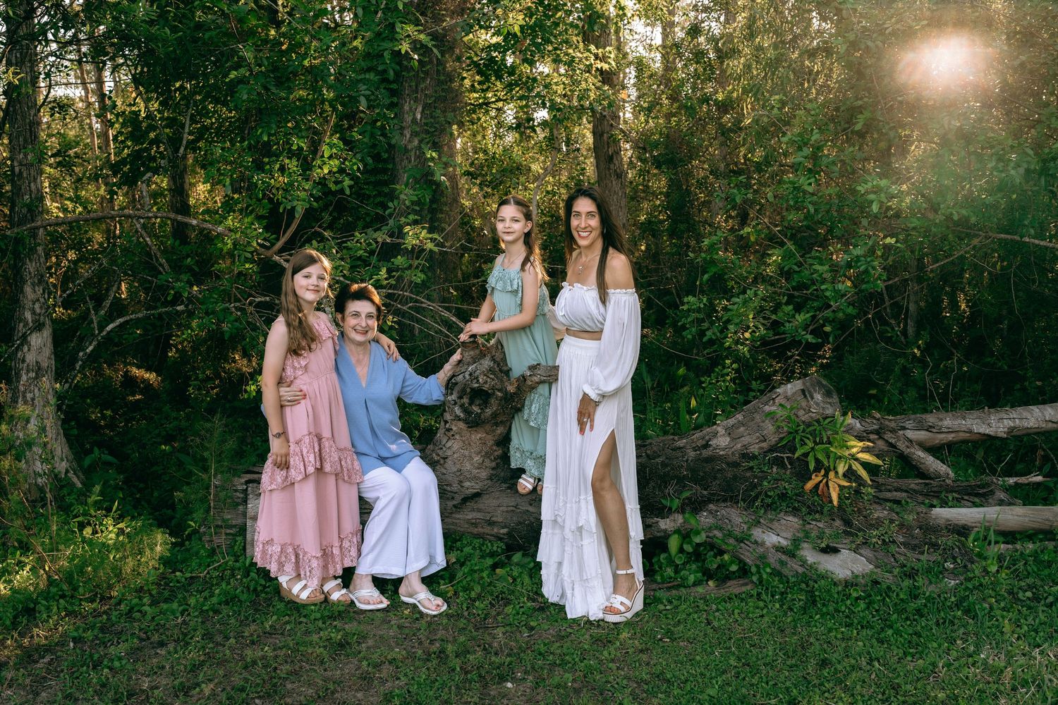 Family of four posing outdoors near a fallen log surrounded by lush green trees in golden hour light. Colt Farms