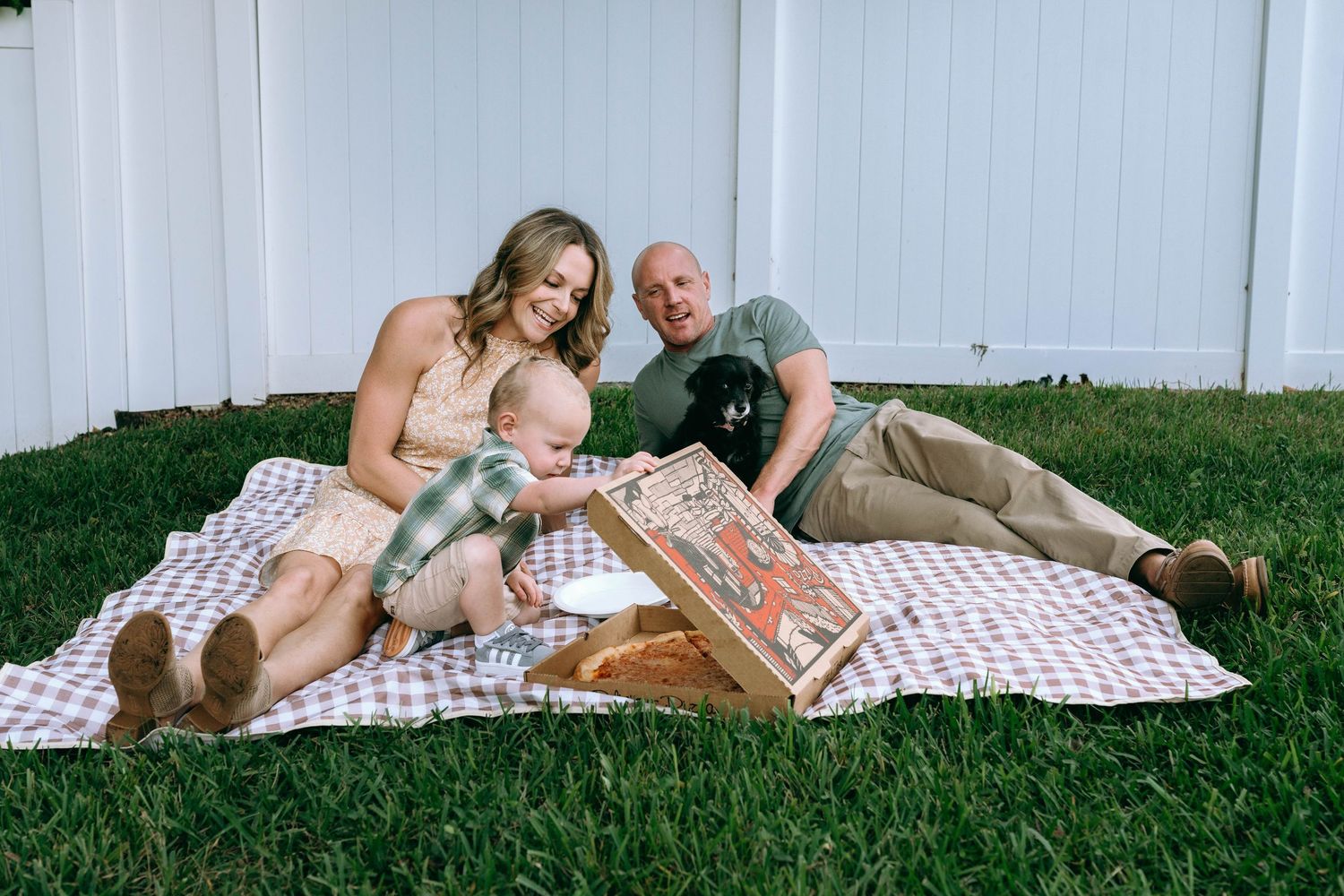 Family relaxing together on a picnic blanket in their backyard.