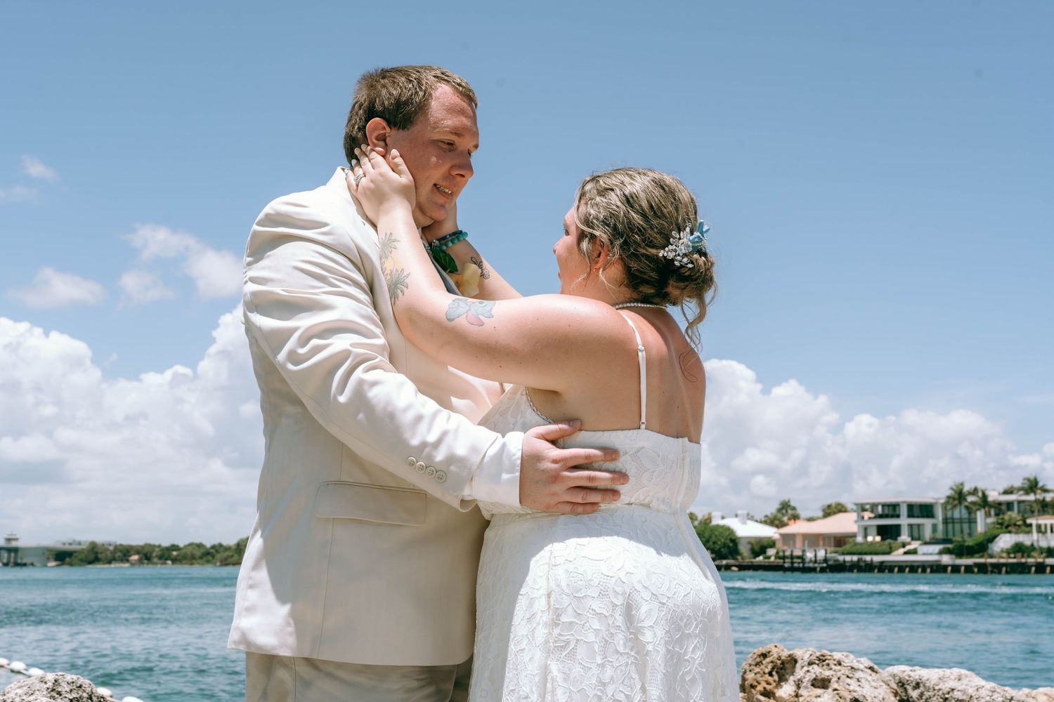 Bride and groom share romantic embrace by the ocean on their sunny beach wedding day.