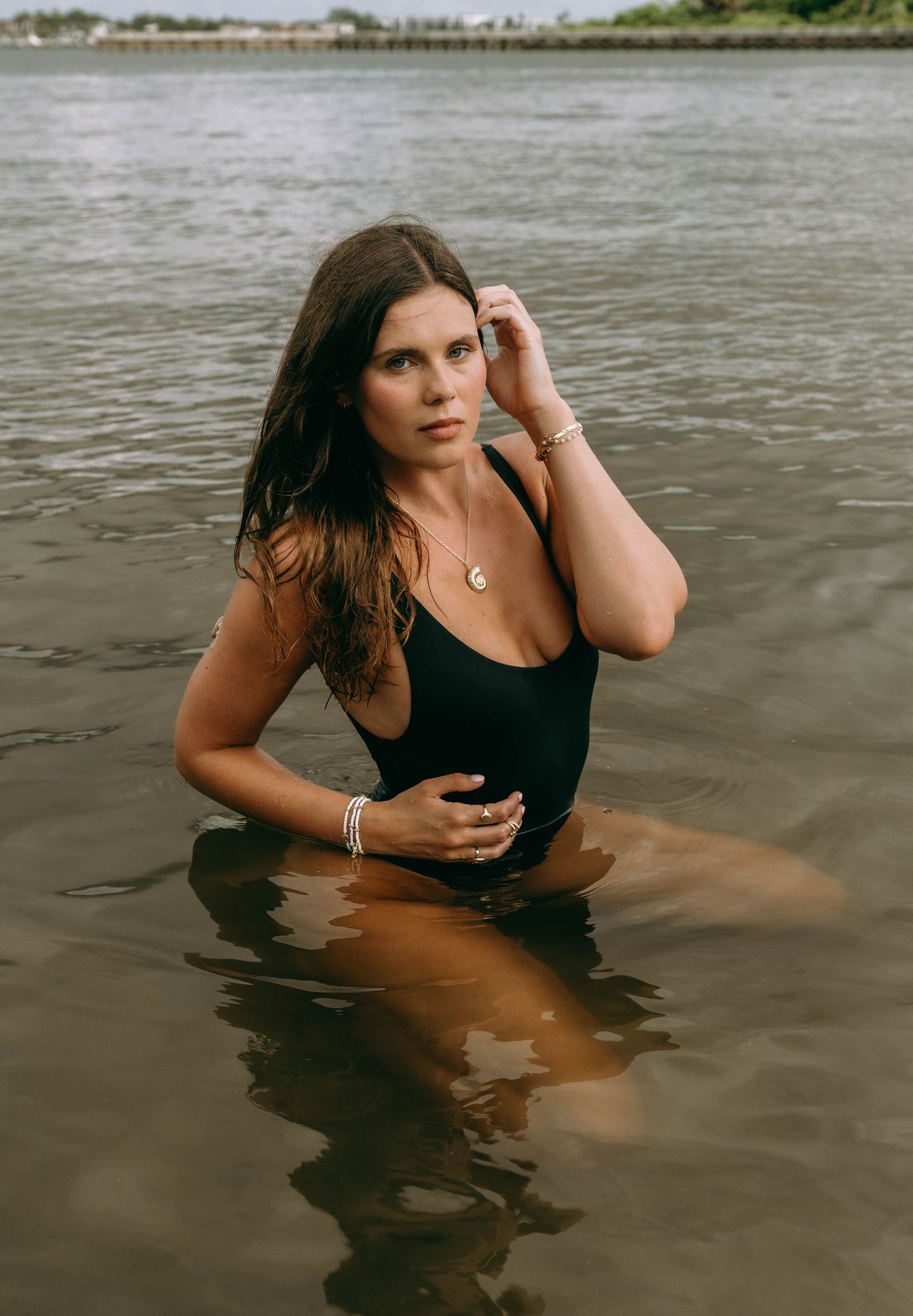 Woman in black swimsuit standing in calm water near shore.