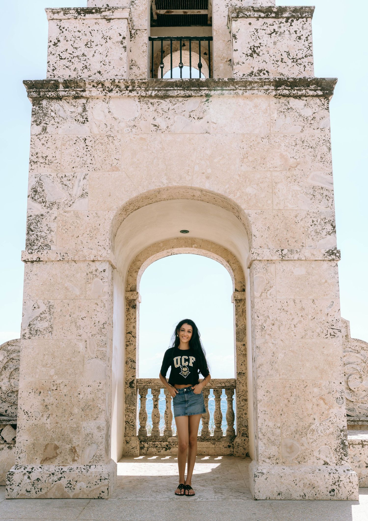 Young woman in UCF shirt standing under historic stone archway with ocean balcony on Worth Avenue Palm beach.