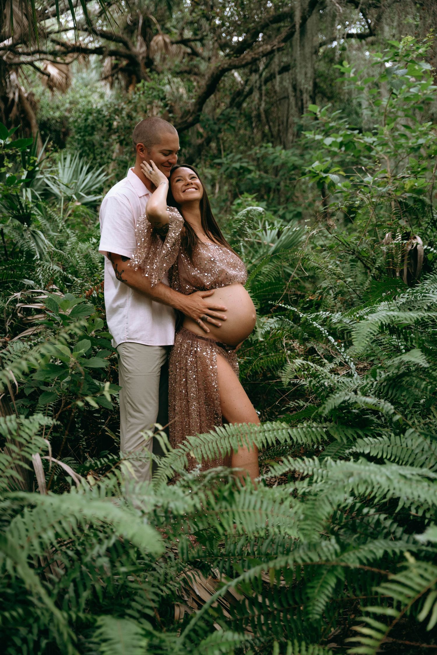 A couple shares intimate moments in a lush tropical garden setting with ferns and palm trees.