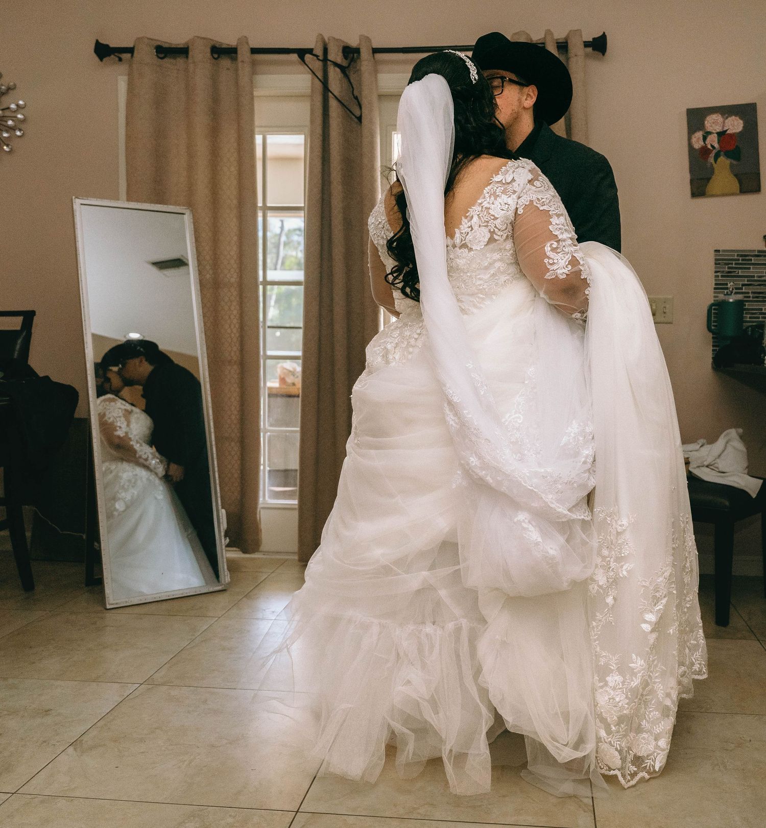 A romantic wedding moment captured in a mirror reflection showing an elegant lace dress and cowboy hat.