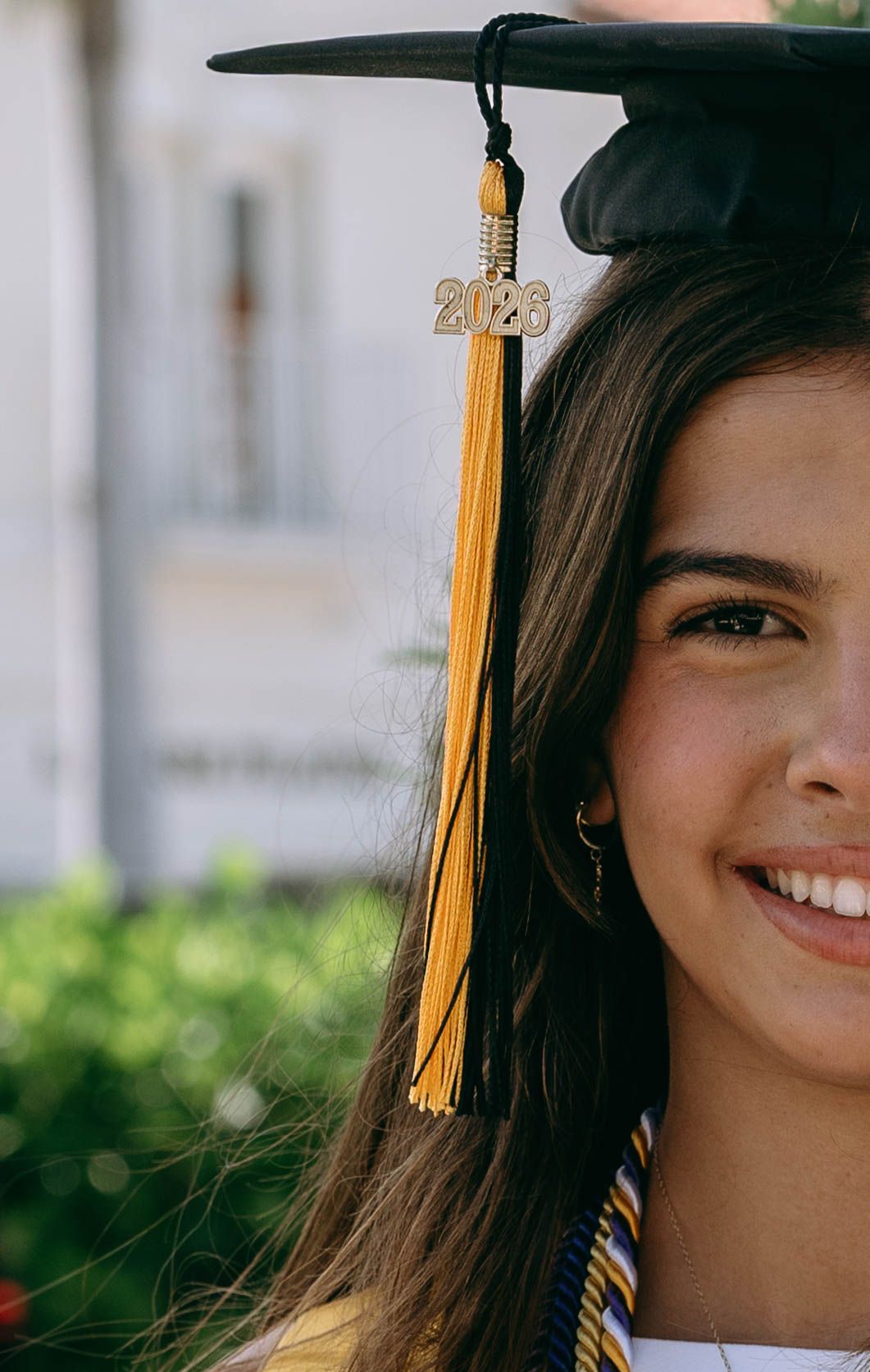 Smiling young woman in black graduation cap with gold 2023 tassel celebrating her academic achievement outdoors on Worth Avenue Palm beach.