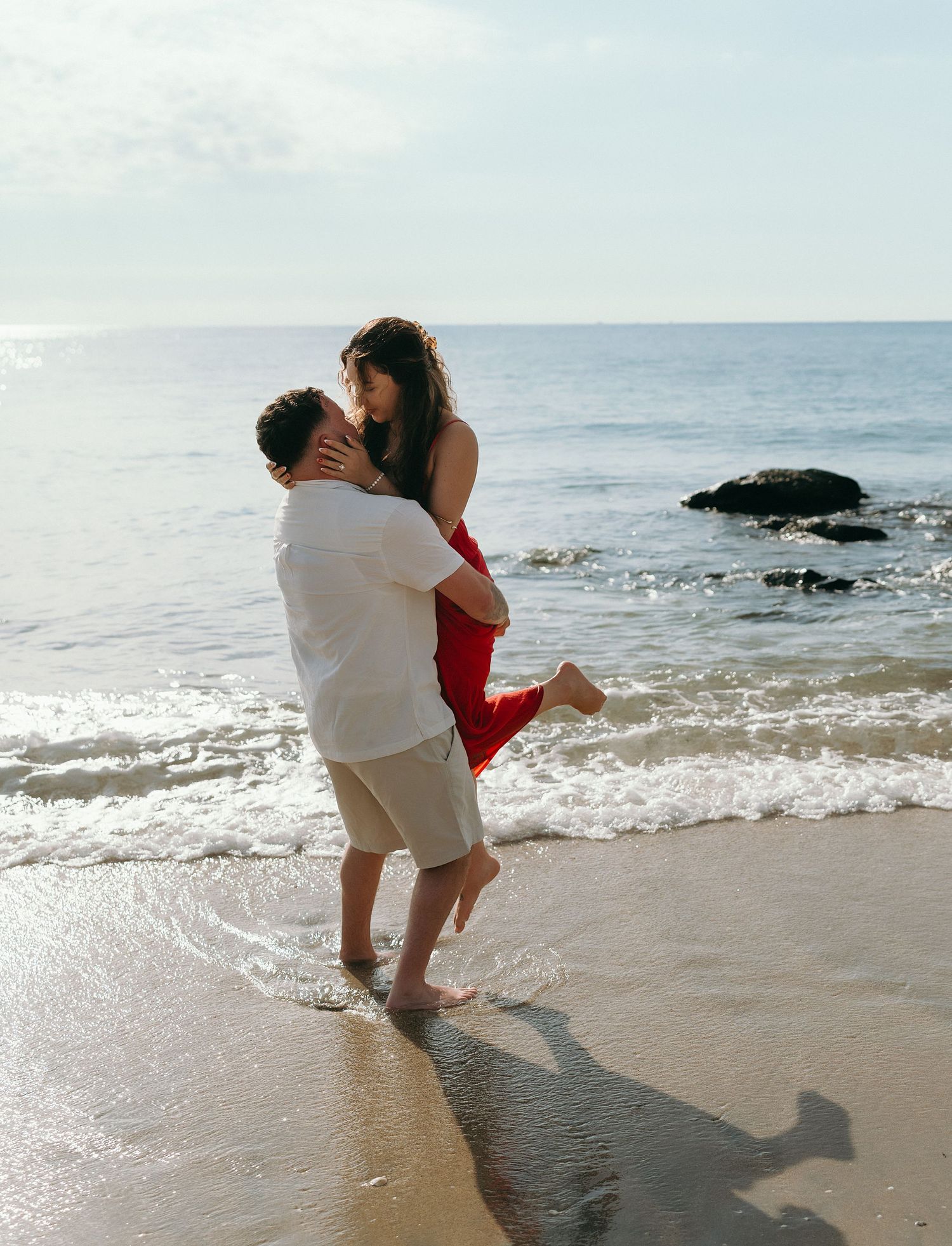 Couple in white and red playing in the ocean waves at sunset.