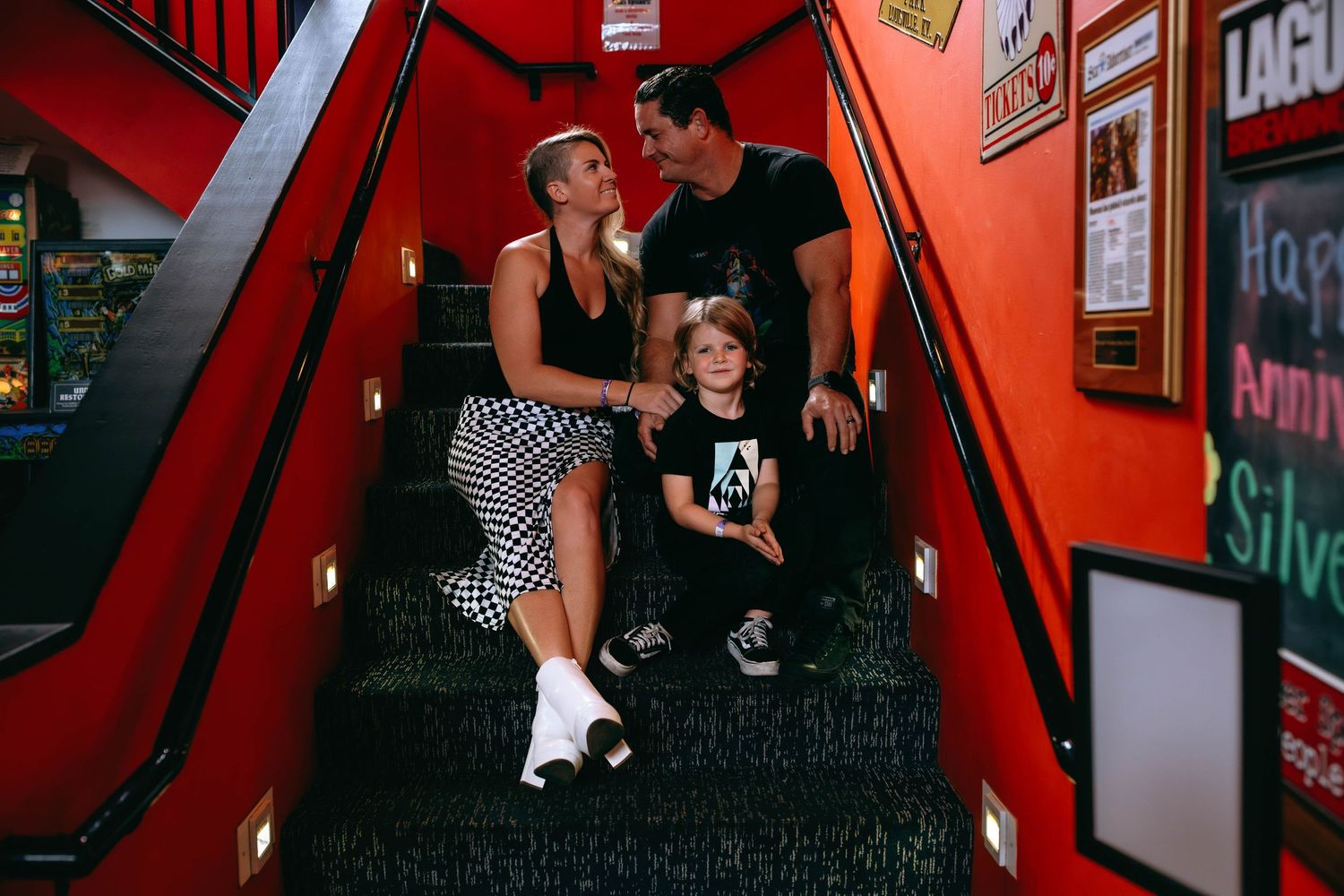 Family of three sitting on red staircase steps, parents with young child in casual black and white outfits.