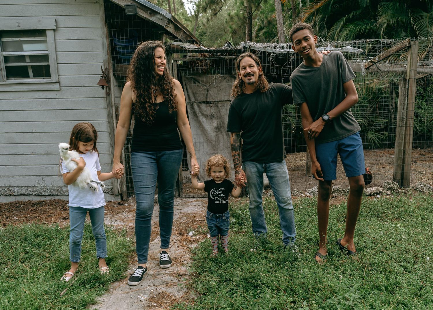 Family of five smiling together outdoors near a rustic fence, enjoying a casual day outside.