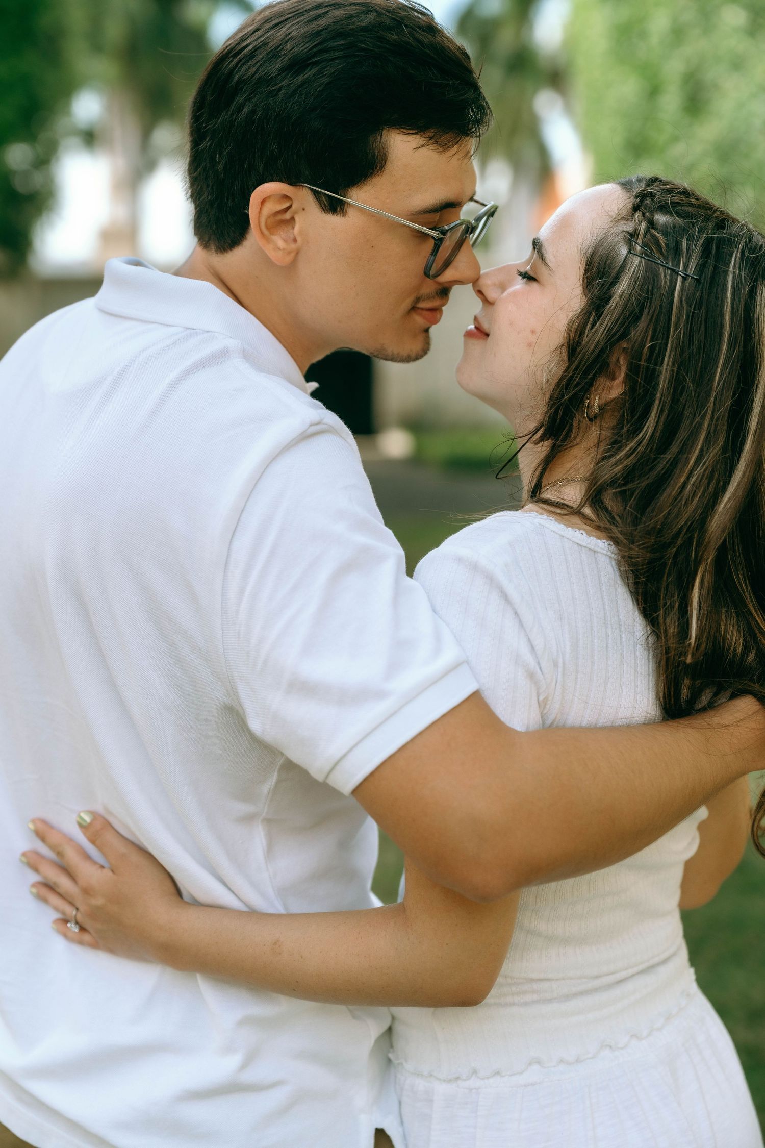 A couple in matching white outfits share a romantic moment, leaning in for a kiss outdoors. Engagement photos on Worth Avenue in Palm Beach