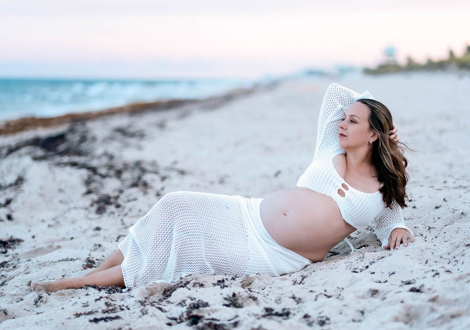 Maternity beach photos with person lying in white dress on sand.