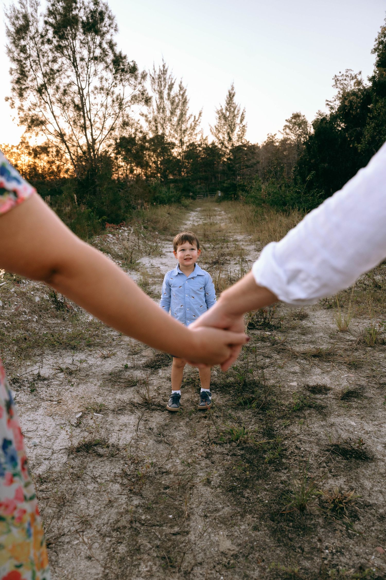 Family members hold hands while walking together on a sandy outdoor path.