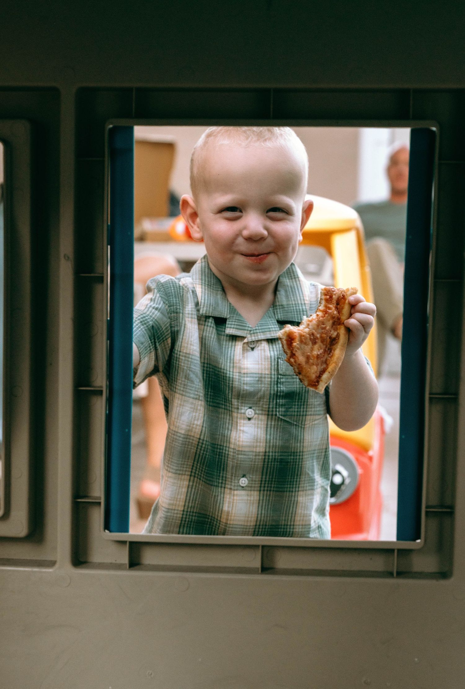 Child holding up food while smiling through window bars.