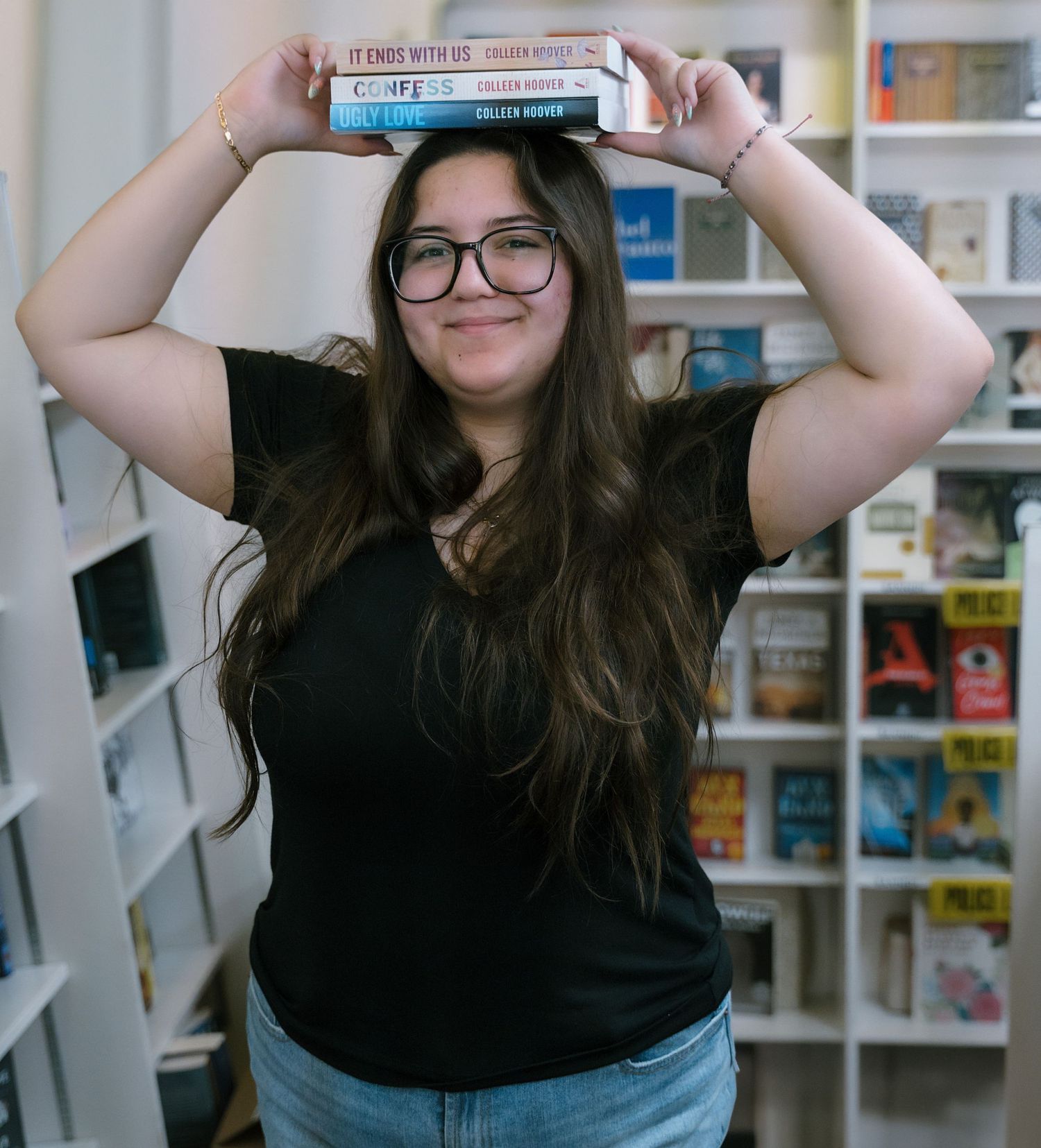 A person balances books on their head while standing in a library.