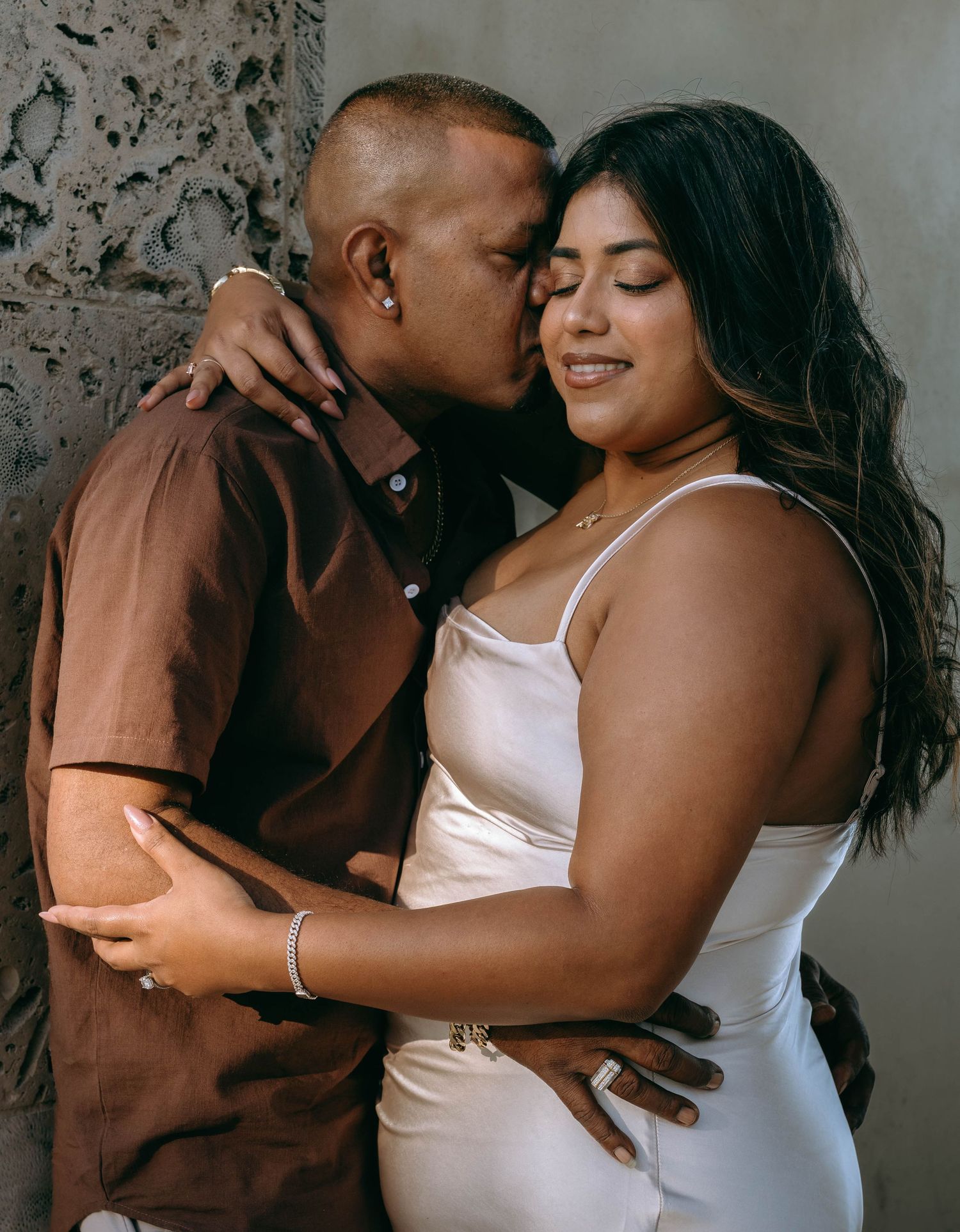A couple shares a tender moment, man kissing woman's cheek as she smiles, dressed in brown shirt and white dress on Worth Avenue Palm beach